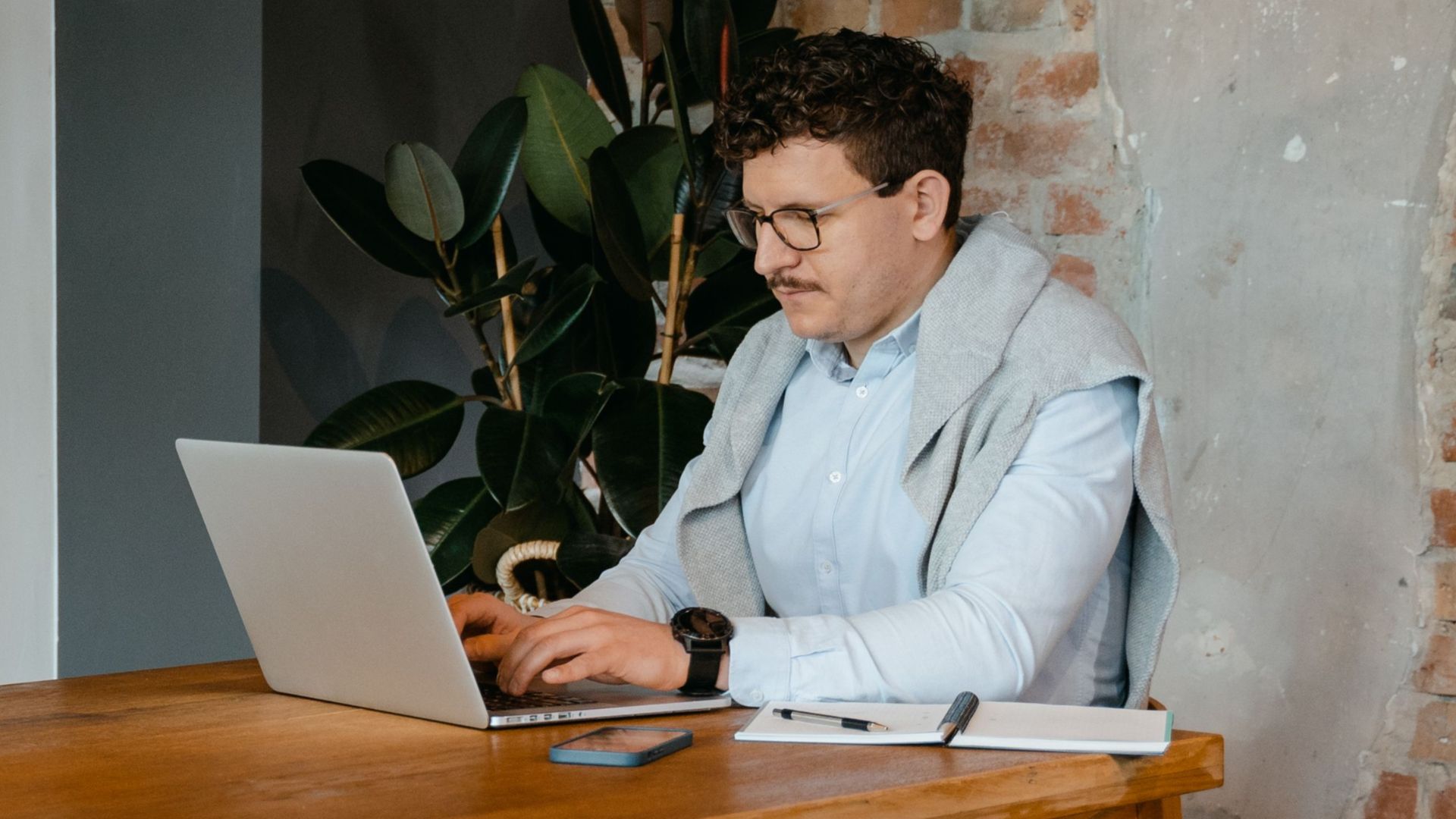 A man working remotely on his laptop in a modern industrial-style workspace.