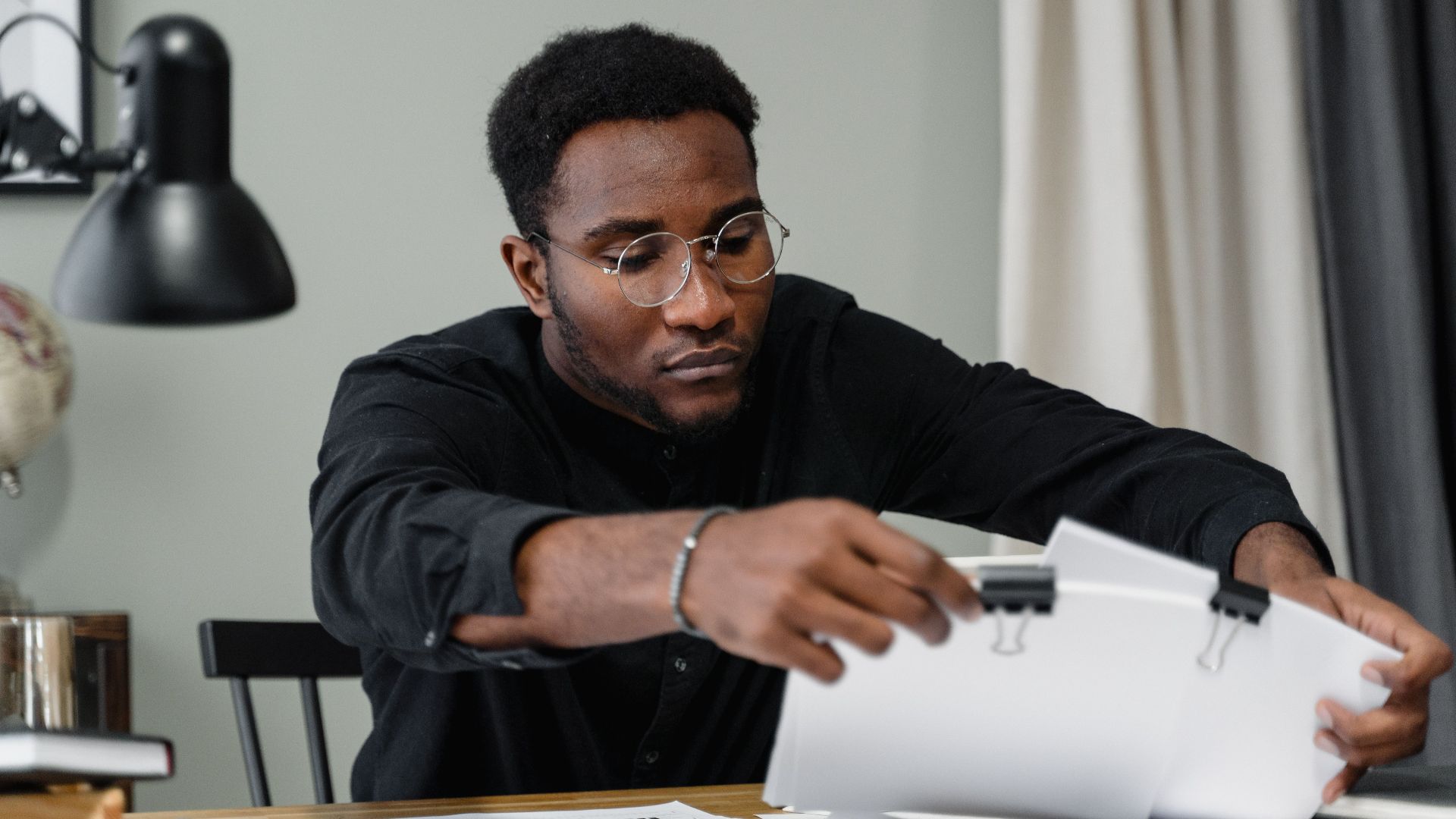 Professional man with glasses reviews documents at a desk in an office setting, emphasizing concentration.