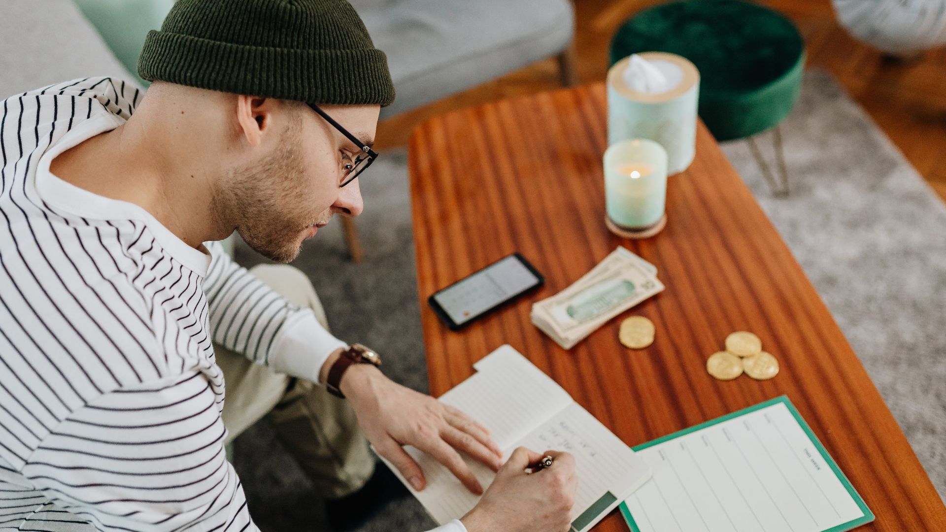 Adult man writing notes at a wooden table with a notebook and accessories.