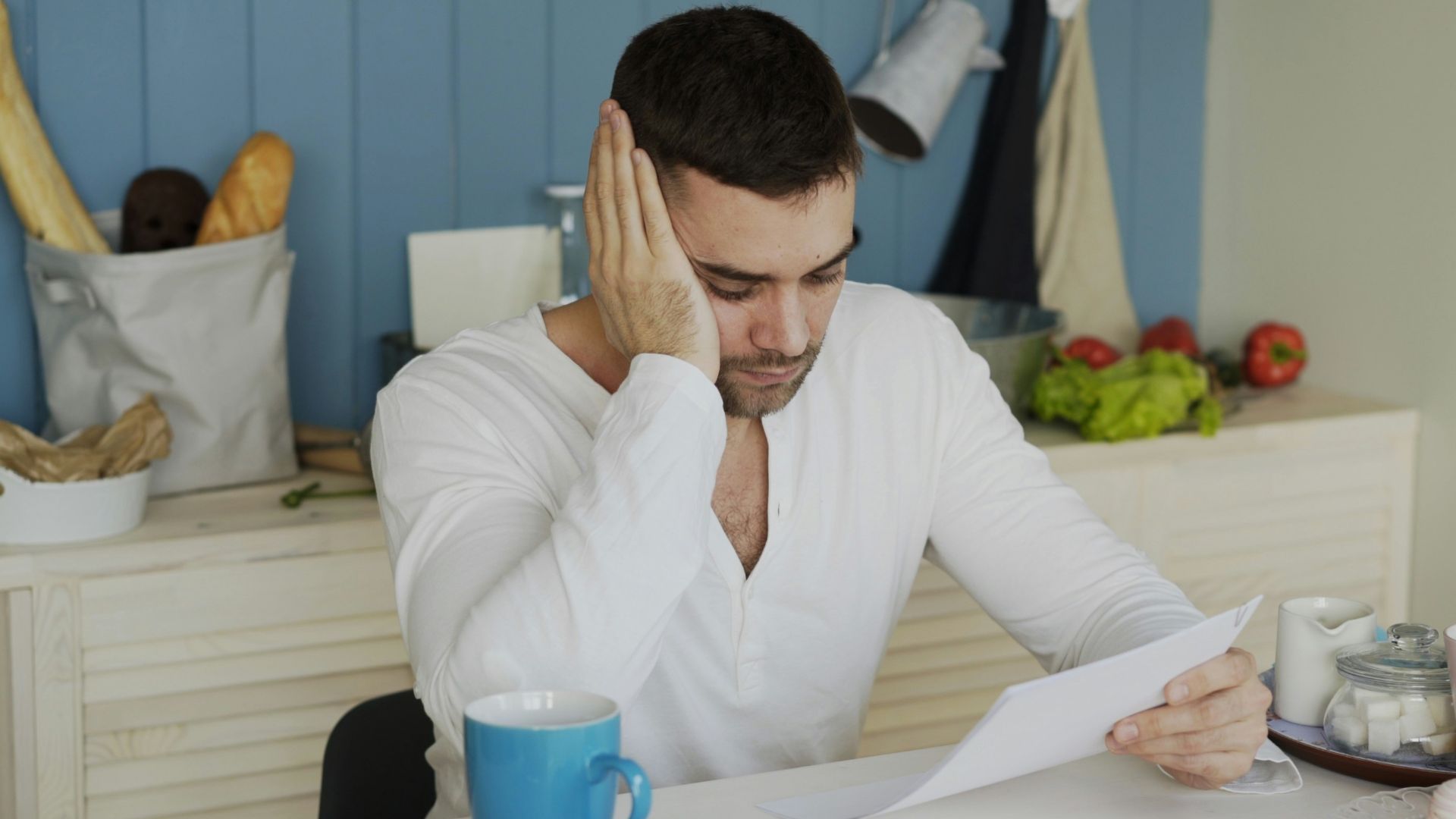 Man sitting at table reading papers with breakfast.