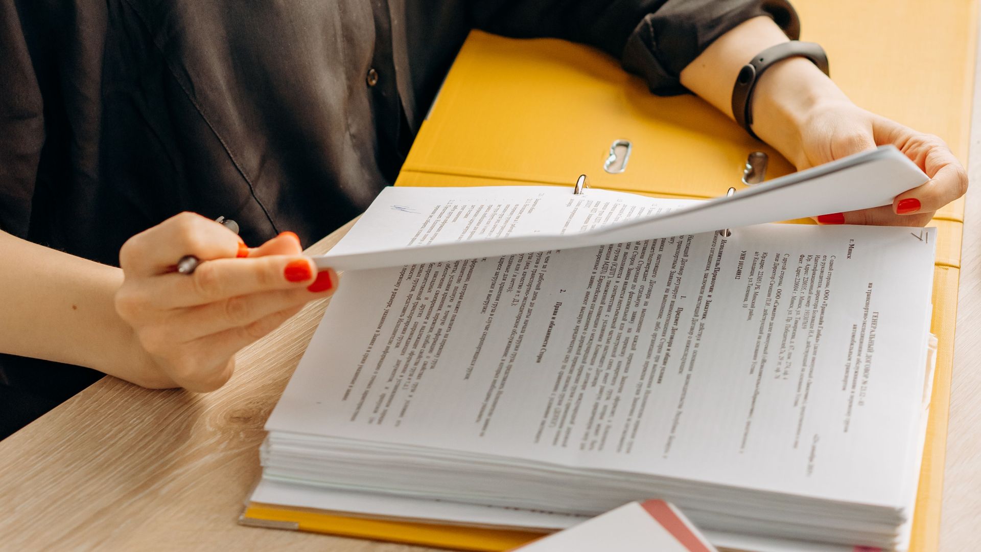 A woman in glasses sits at a desk reading documents in a modern office.