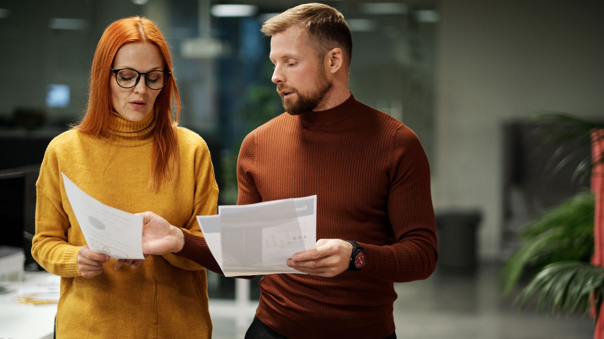 Two professionals in modern office discussing documents, reflecting collaboration and teamwork.