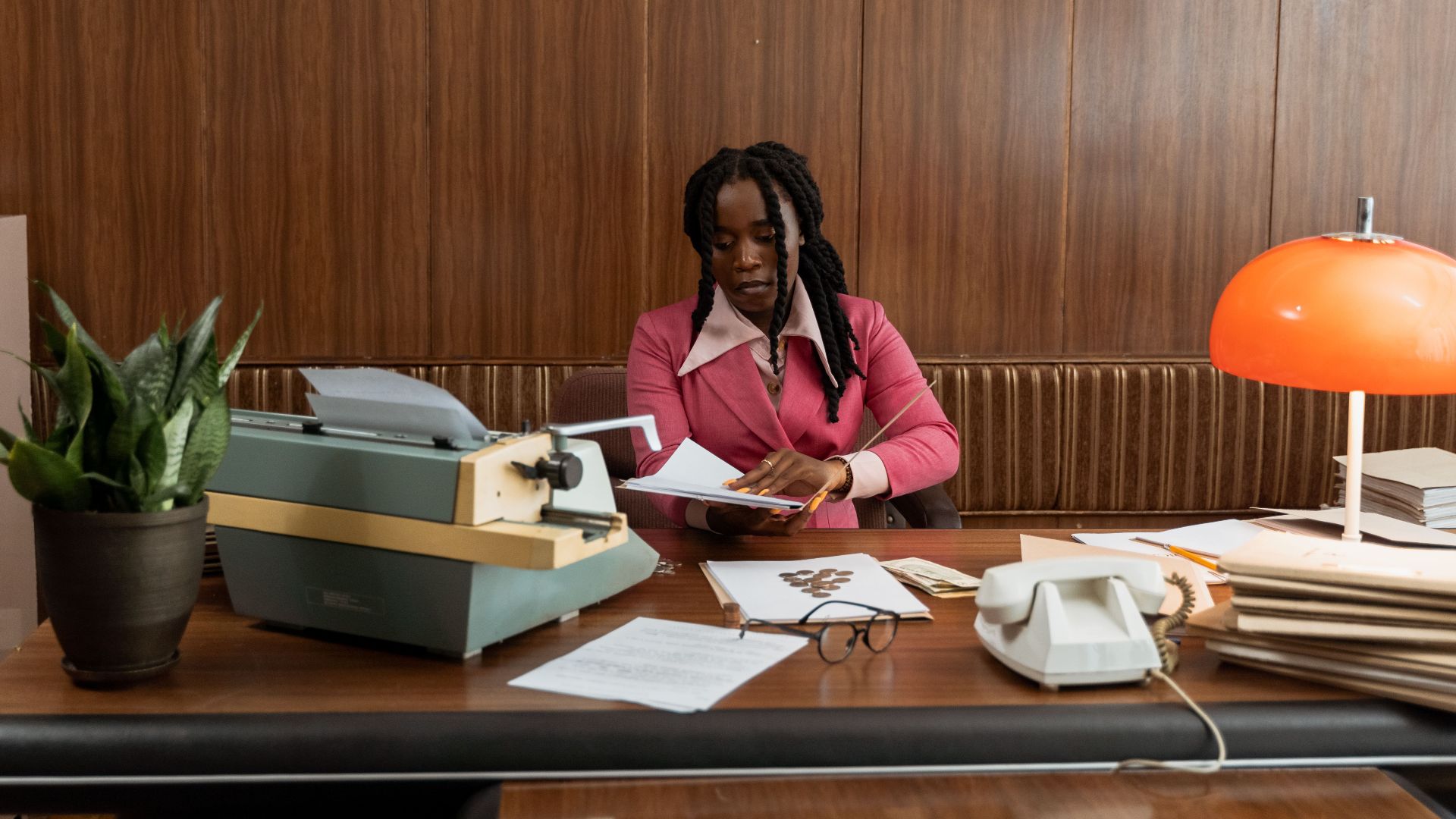 A businesswoman in a pink blazer works at a vintage desk with a typewriter and retro decor.
