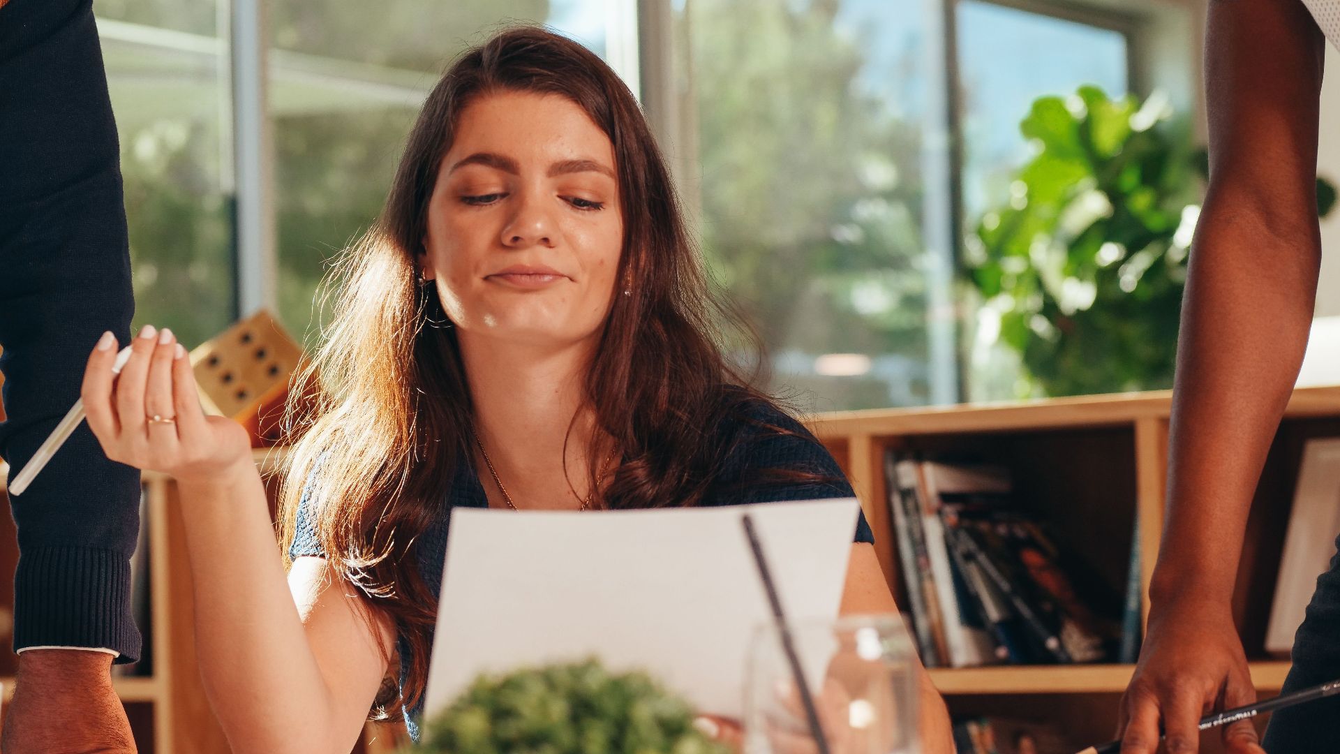 Confident businesswoman analyzing documents in a modern office setting with colleagues.