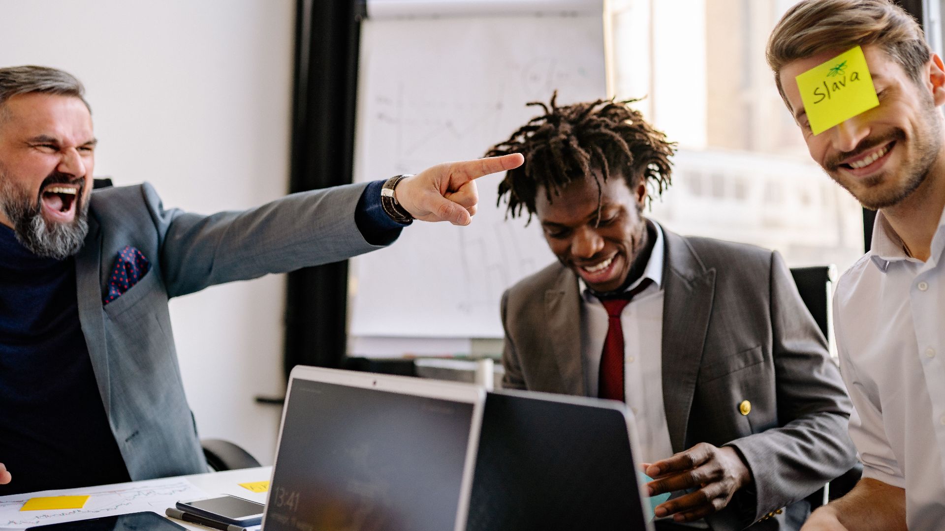 Three diverse colleagues enjoy a lighthearted moment with sticky notes during an office meeting.
