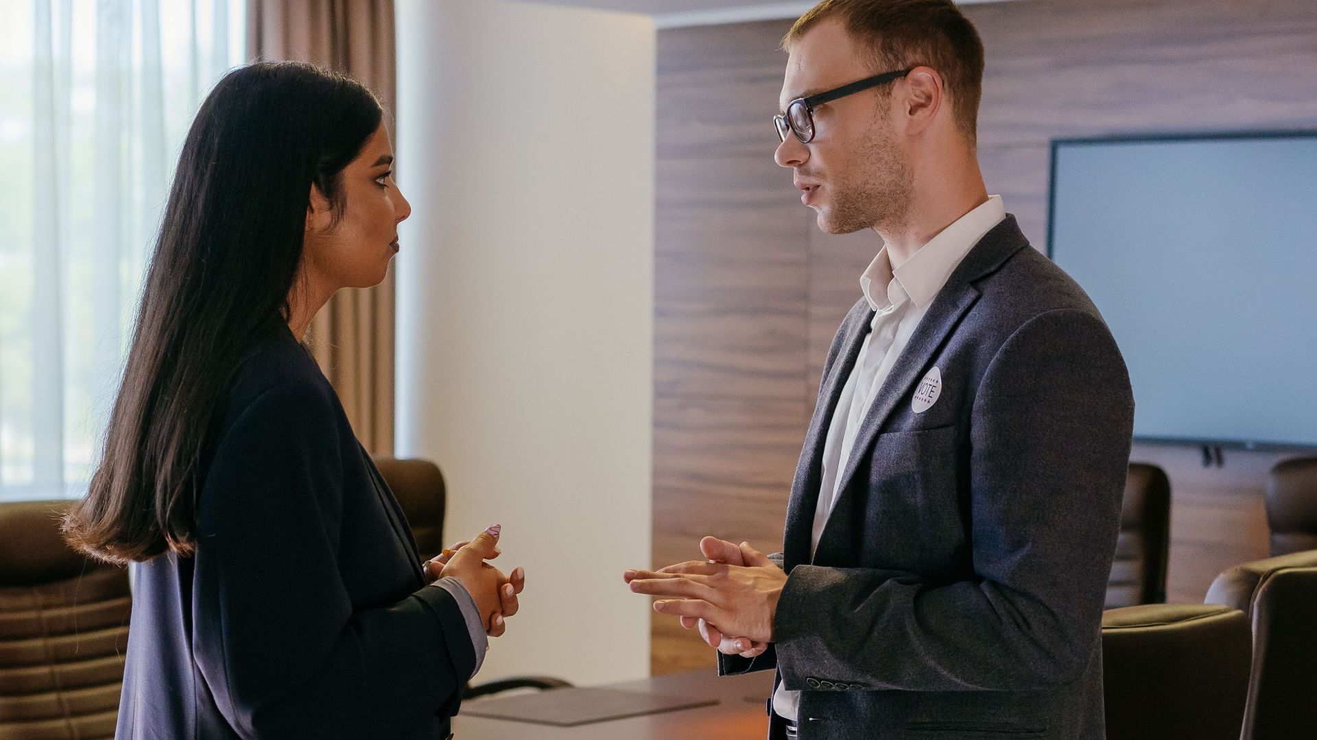 Two professionals engaged in discussion inside a modern conference room setting.