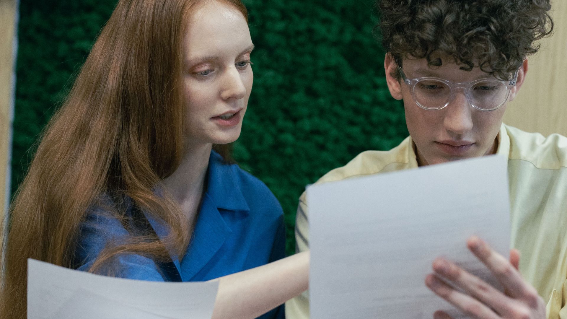 Two young adults studying documents together in an indoor setting, focused on learning.