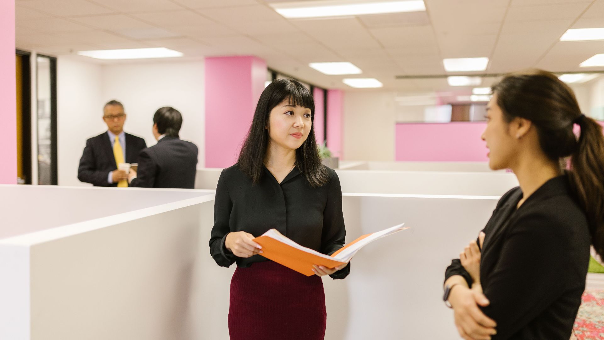 Two businesswomen discuss documents in a modern office setting, highlighting teamwork and professionalism.