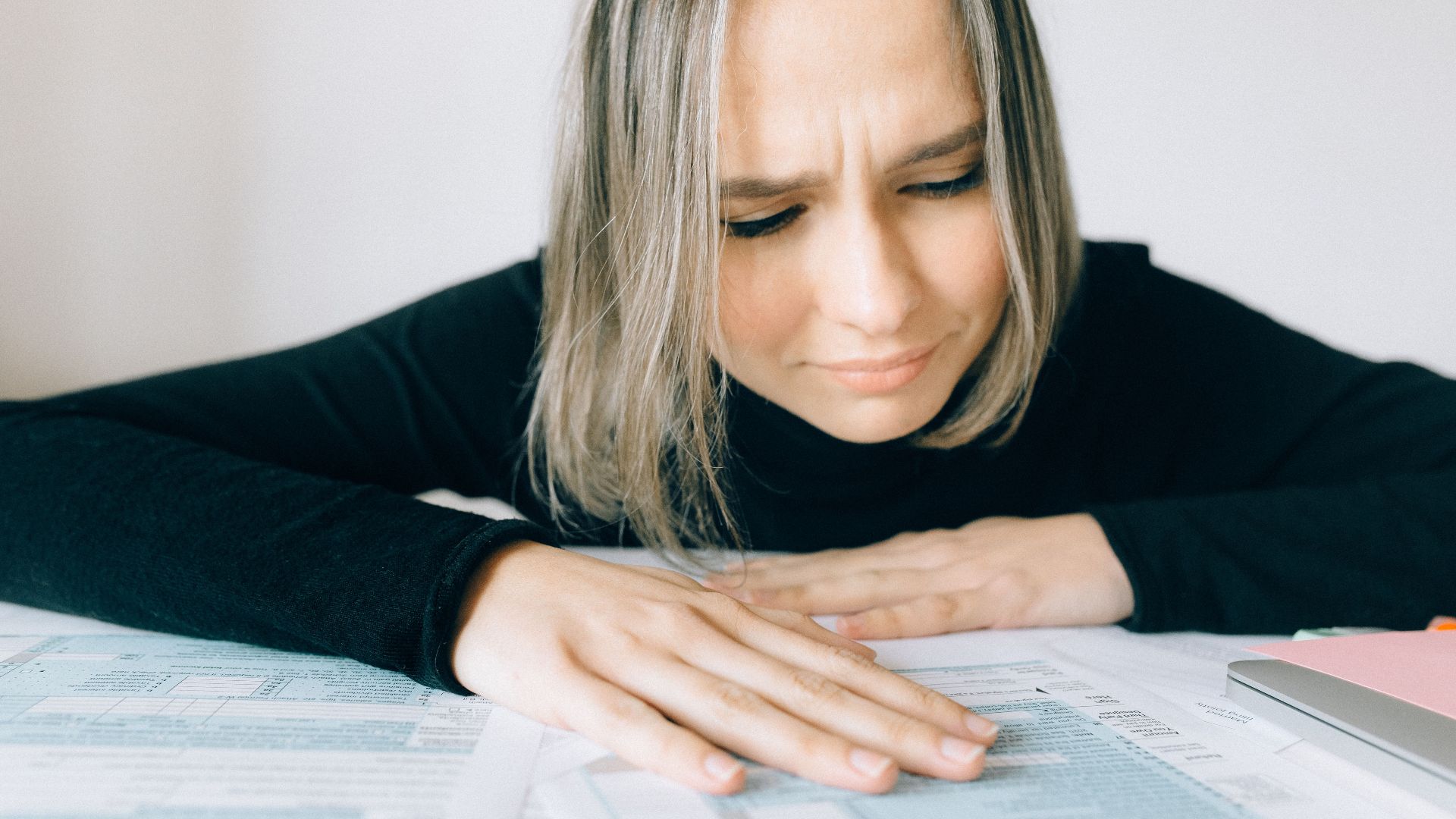 A worried woman analyzing financial paperwork at her desk, signifying stress during tax season.