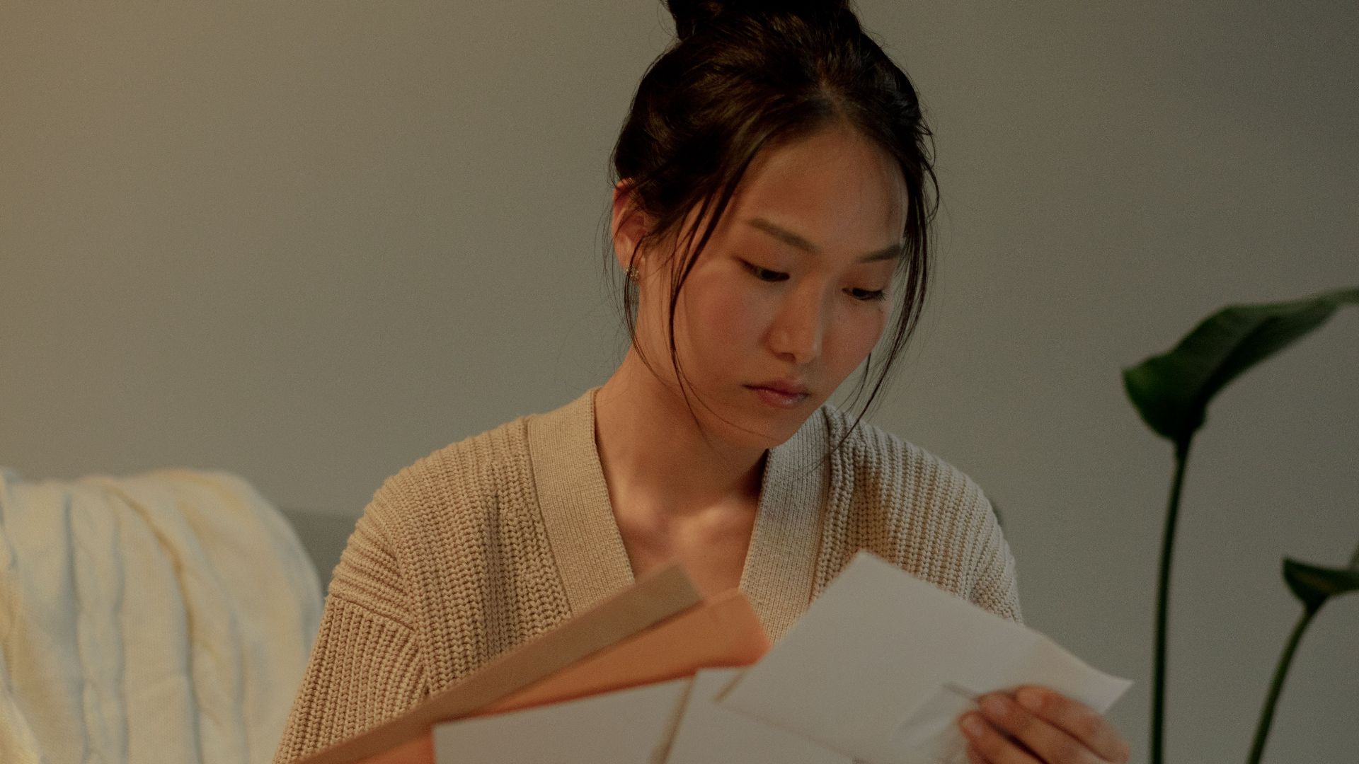 A woman seated in an armchair reads letters with focus, creating a warm, introspective mood.