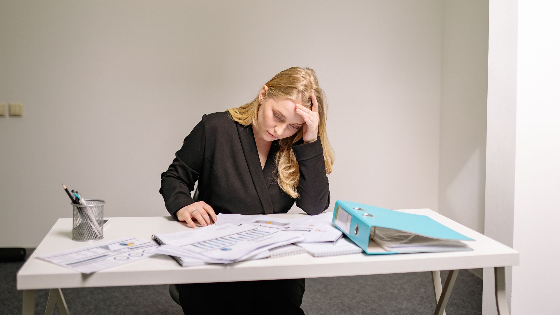 A stressed businesswoman reviewing documents at her desk, overwhelmed by paperwork.