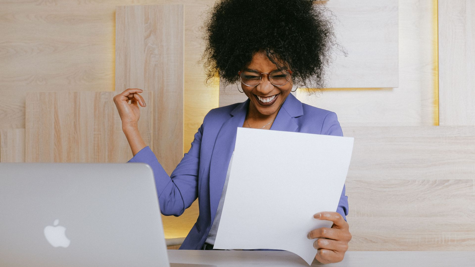 A cheerful woman celebrates her success at work, looking at a document in an office setting.