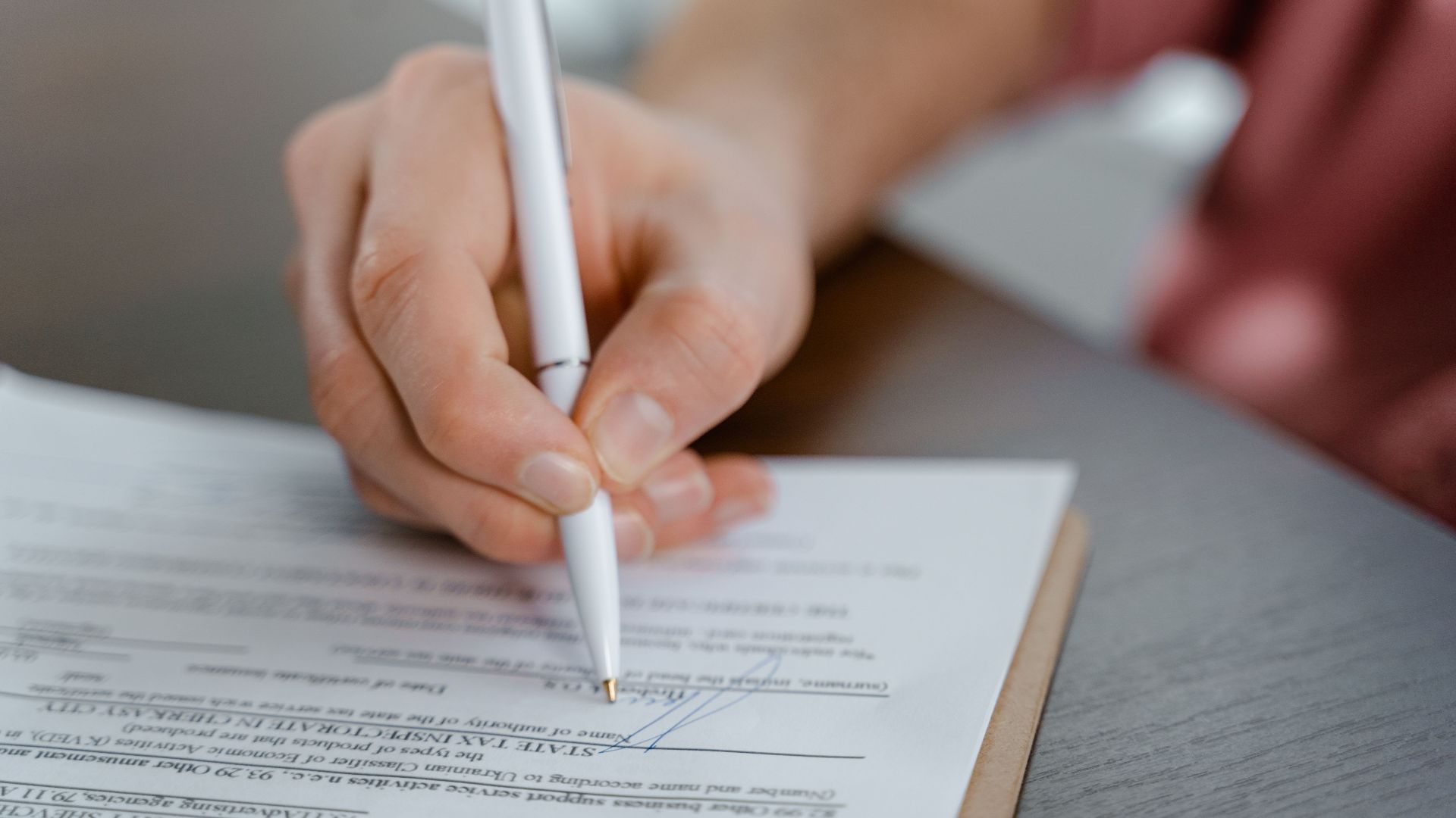 Detailed view of a hand writing a signature on an official document with a ballpoint pen.