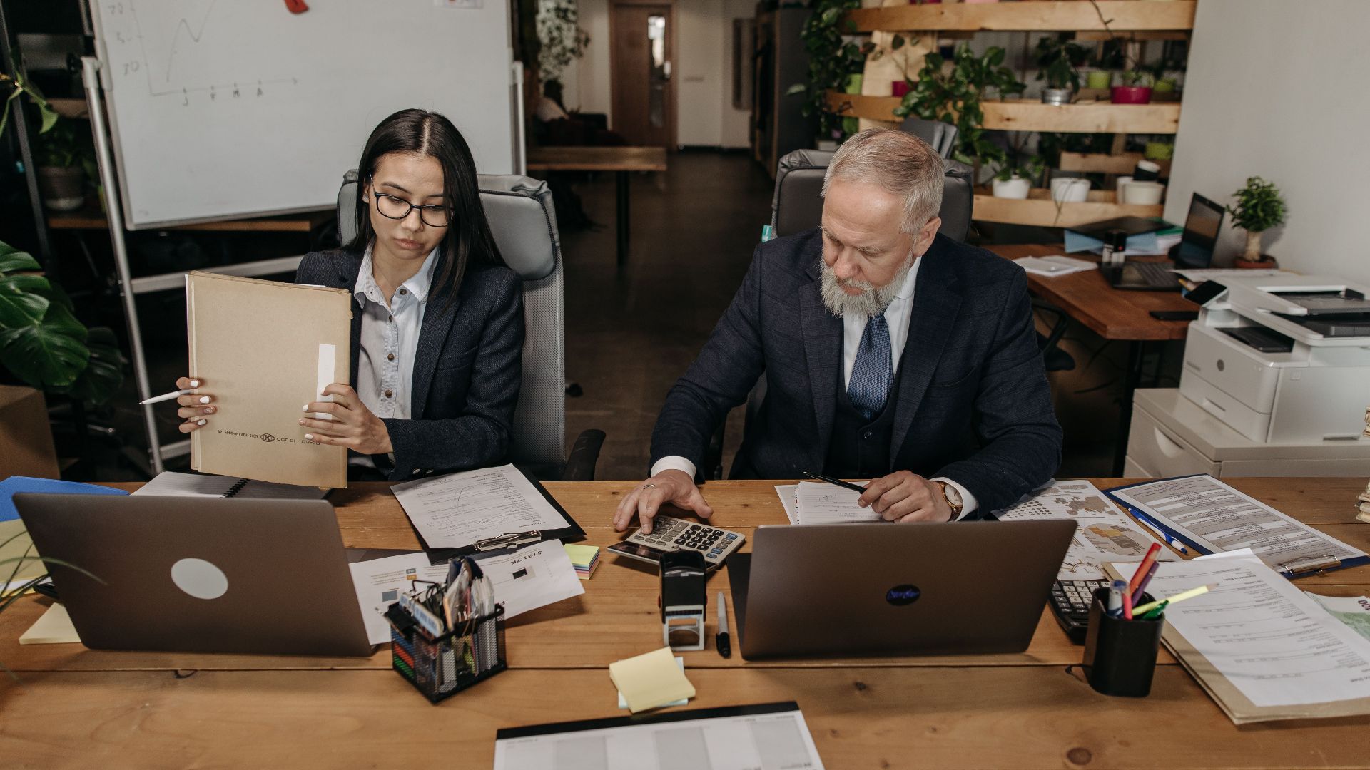 Business professionals in a modern office working collaboratively at desks with laptops.