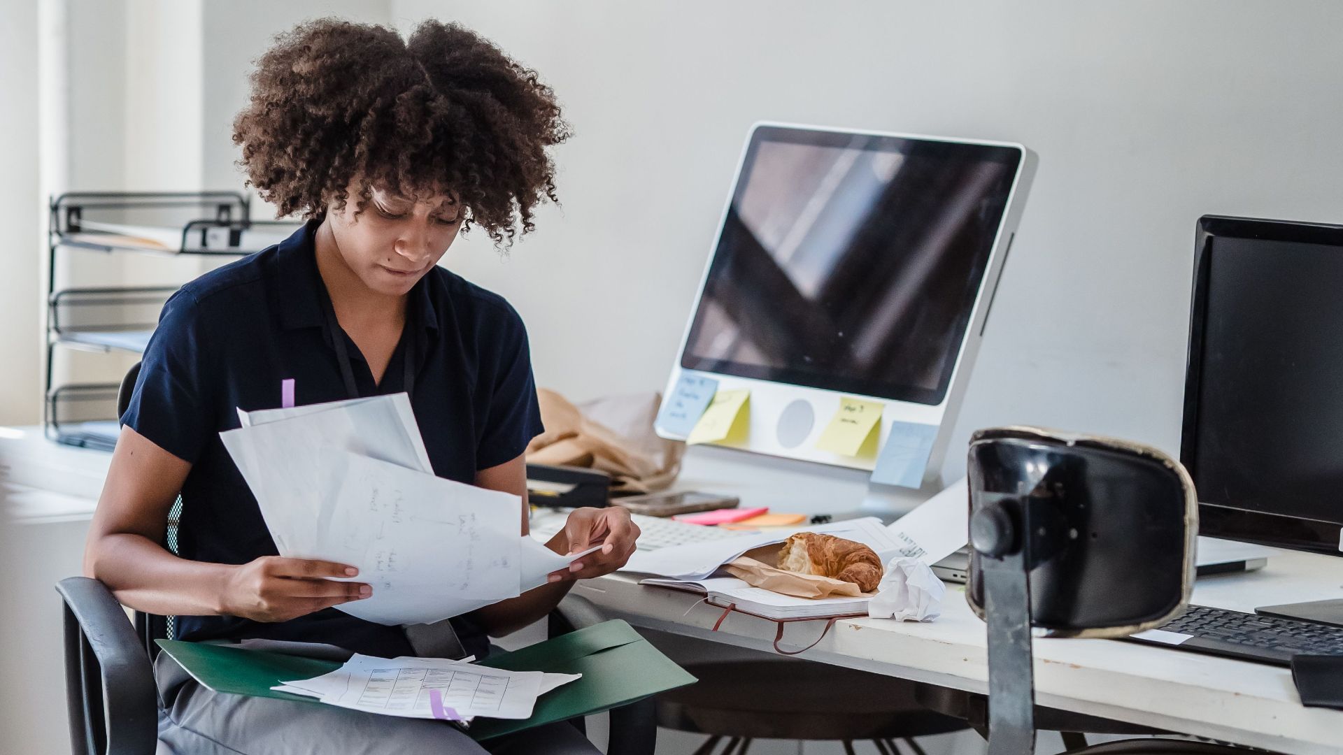 Young businesswoman multitasks with documents and laptop in a modern office setting.
