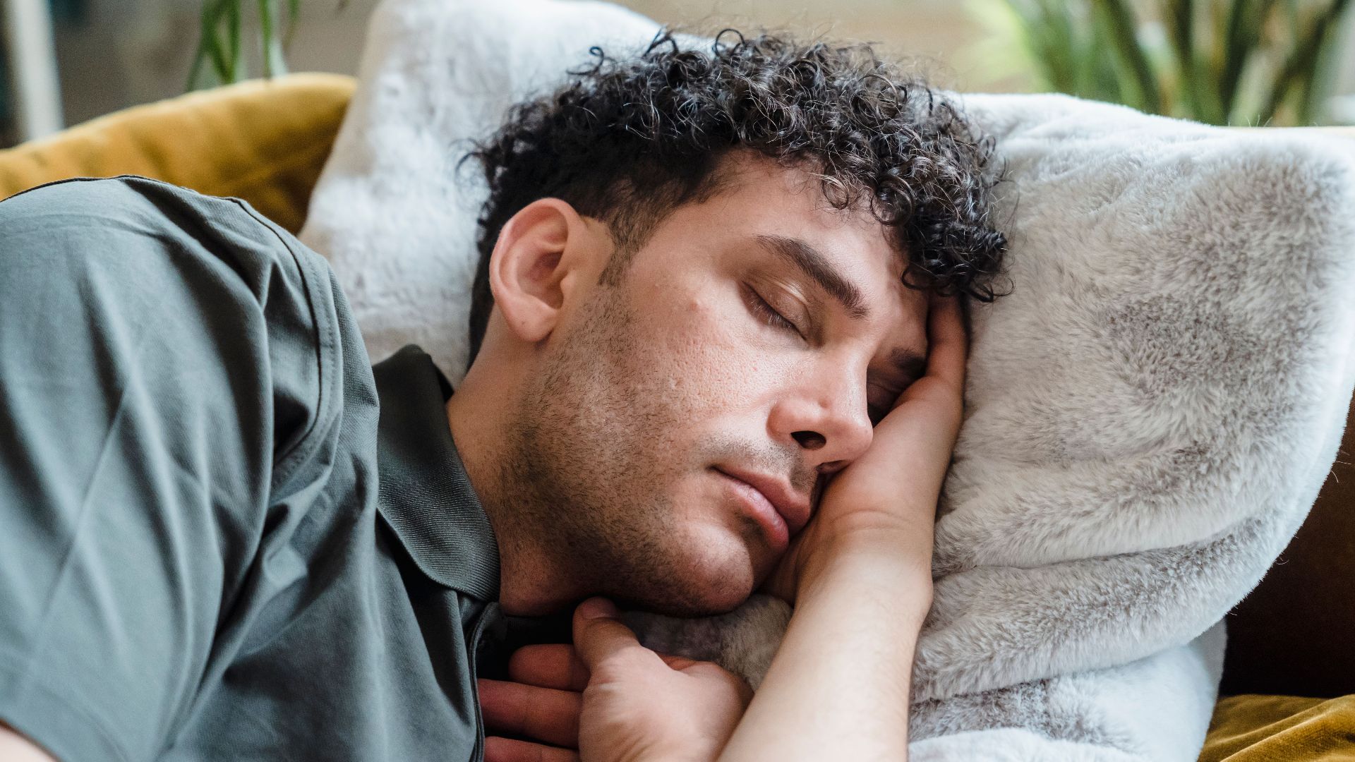 A young man with curly hair peacefully sleeping on a cozy couch with a soft pillow.