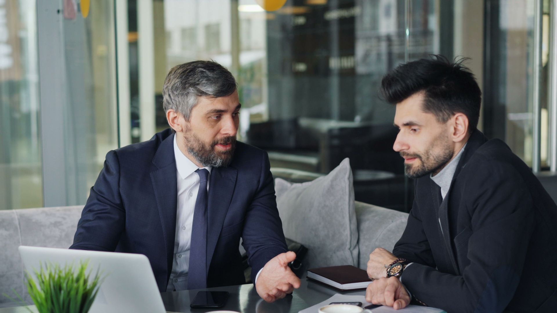 Two businessmen in a café having a professional discussion with coffee and a laptop.