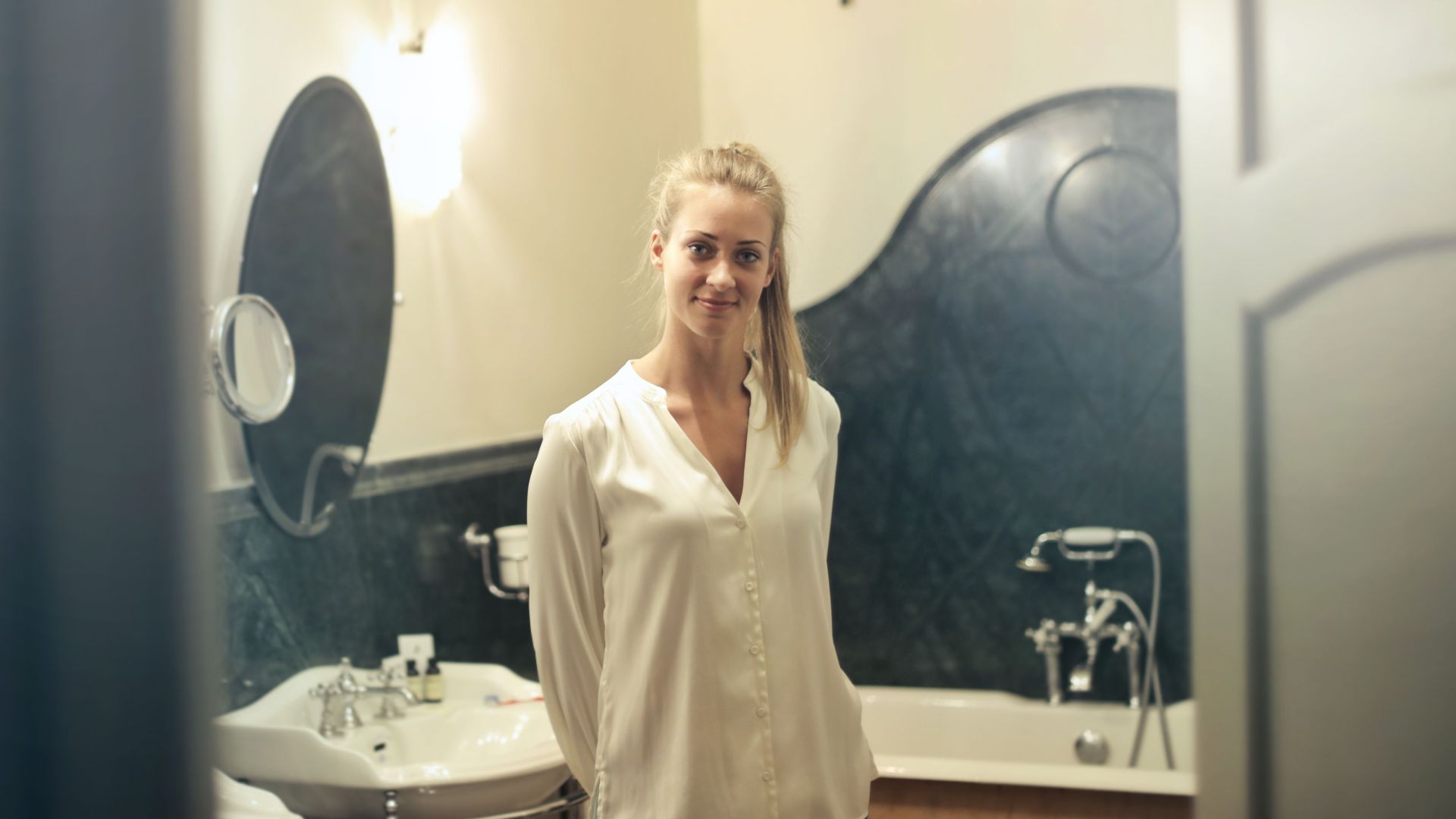 Portrait of a smiling woman in a stylish bathroom setting, showcasing luxurious decor and ambient lighting.