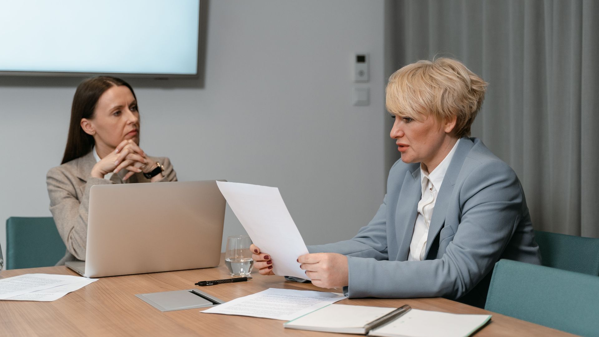 Two businesswomen in a serious meeting, discussing documents with a laptop in an office setting.