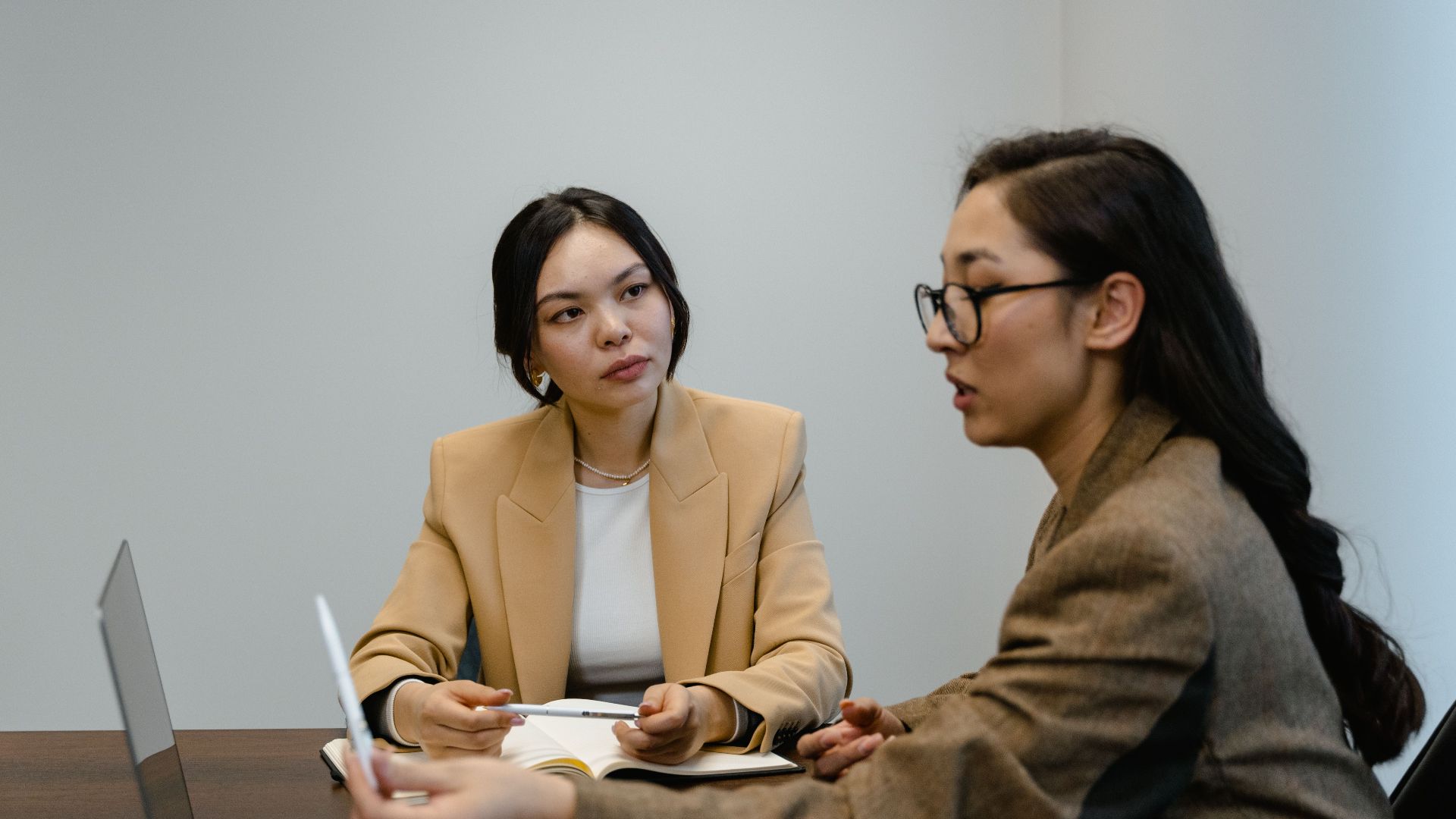 Two Asian businesswomen in a professional meeting discussing work at a conference table.