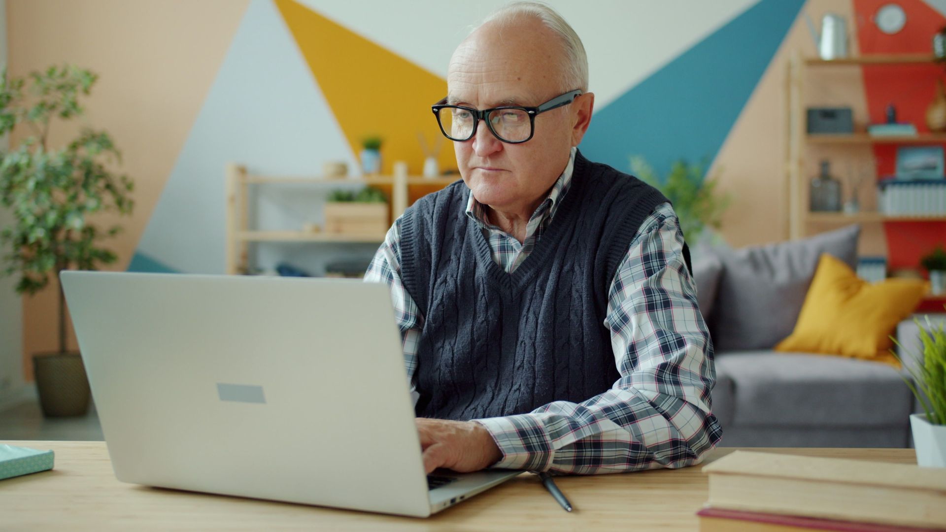 Elderly man using laptop in stylish home office, focused and diligent.