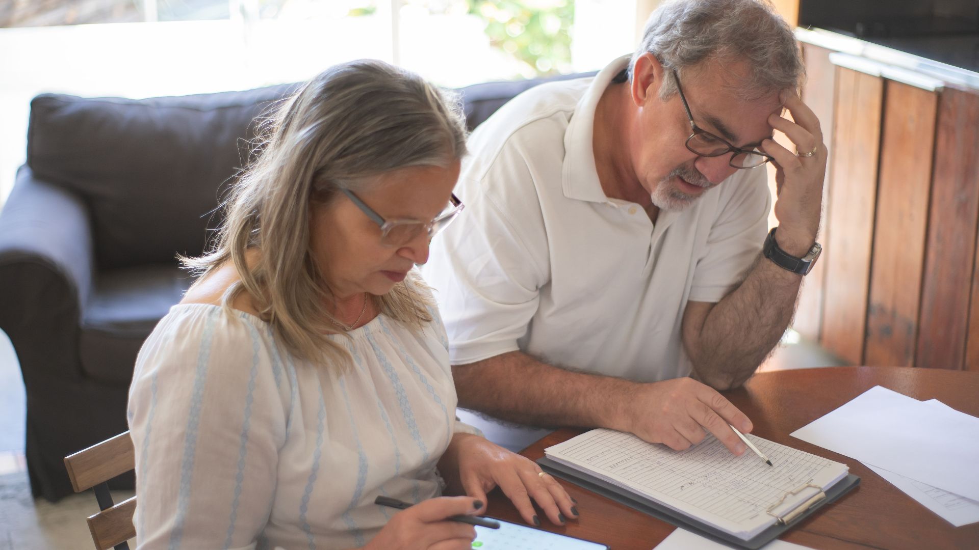 Elderly couple reviewing bills and documents at home, focusing on finances and technology.