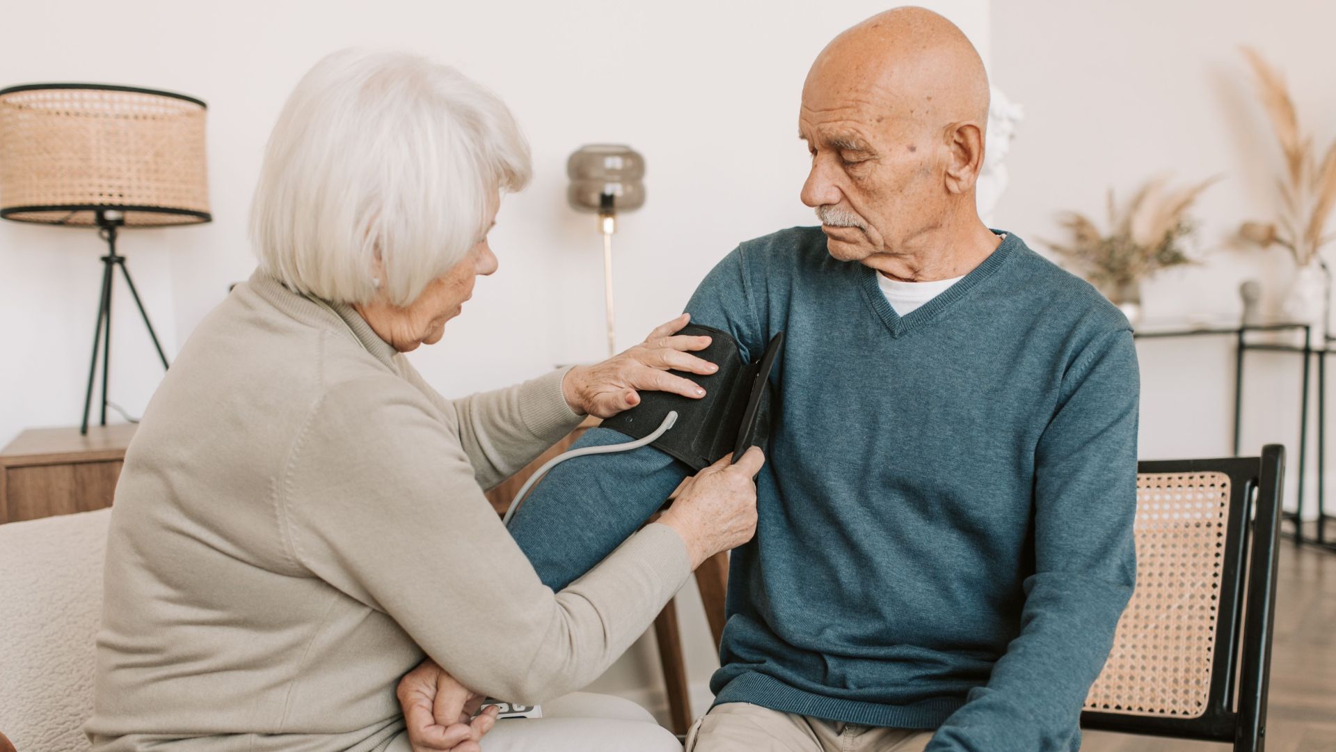 Elderly couple involved in a home blood pressure checkup, emphasizing health and care.