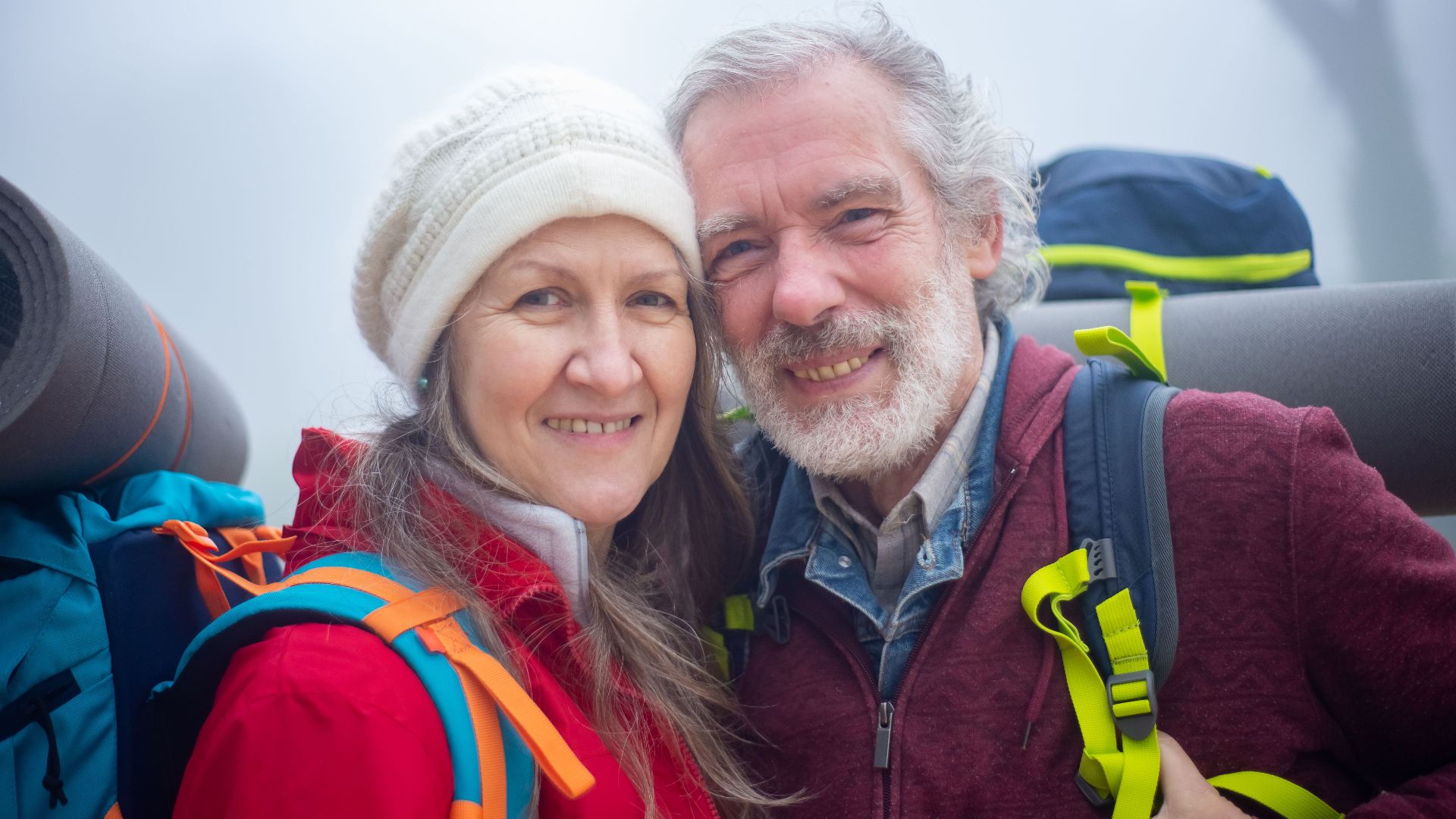 Senior couple hiking with backpacks, smiling in the outdoor misty environment of Portugal.