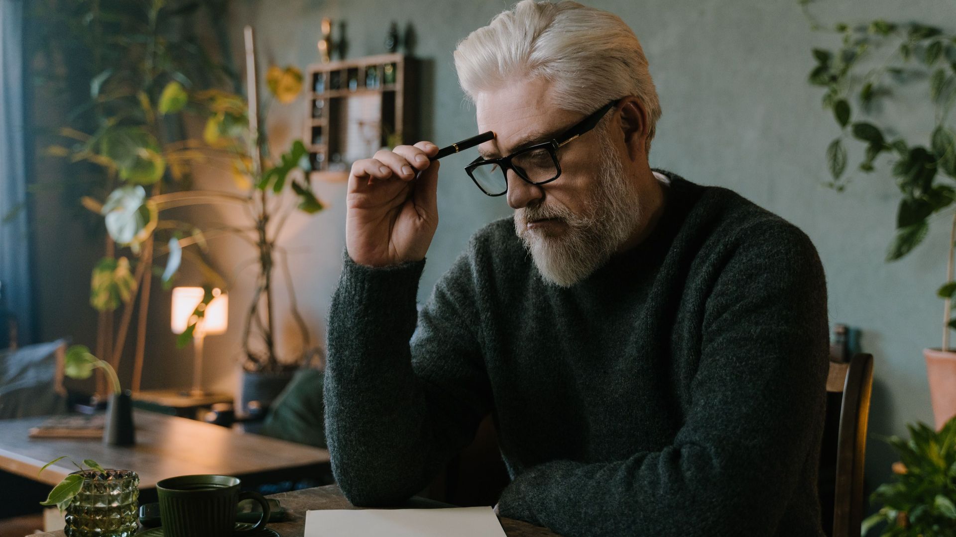 Elderly man with gray hair and beard thinking while sitting at table.