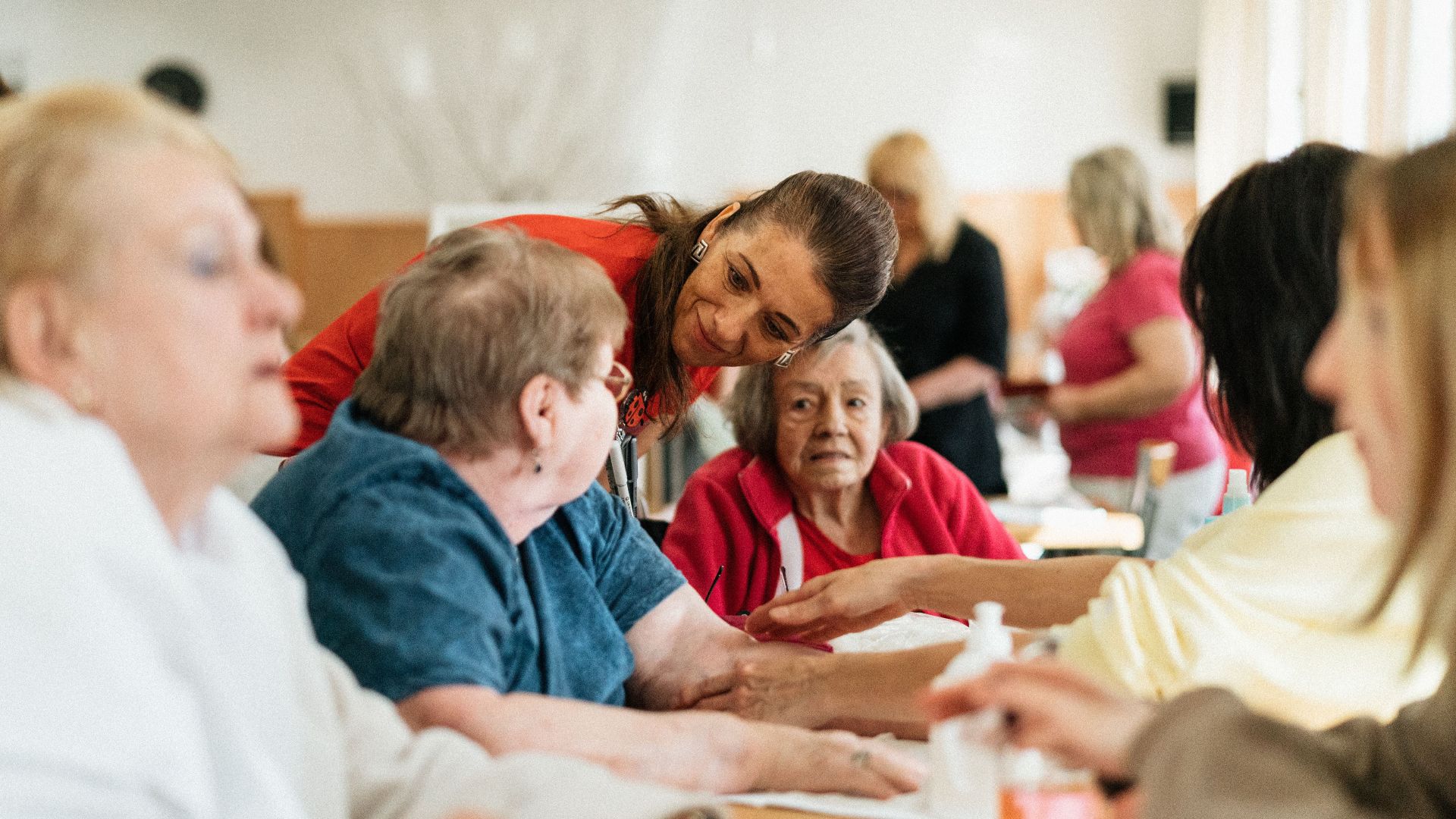 Smiling caregivers and seniors engage over a table at a community center.