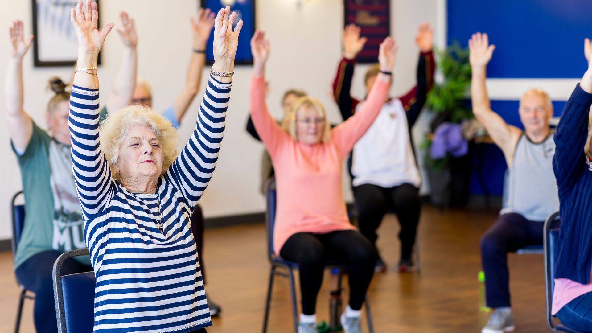 Group of senior adults participating in a chair exercise class, promoting fitness and healthy lifestyle.