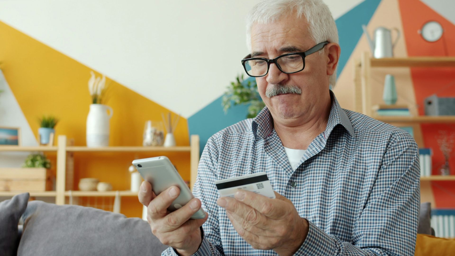 Elderly man using smartphone and credit card for online shopping.