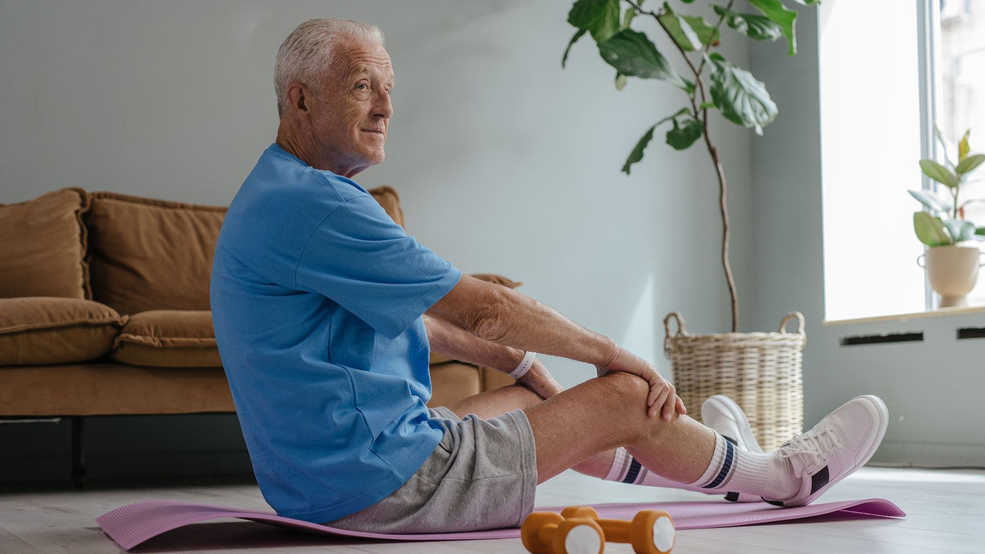 Elderly man exercising at home with yoga and weights for a healthy lifestyle.