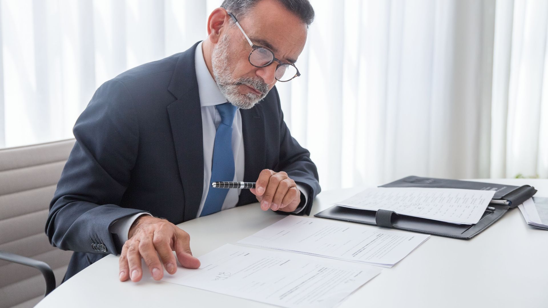Elderly businessman focused on reviewing documents at his office desk.