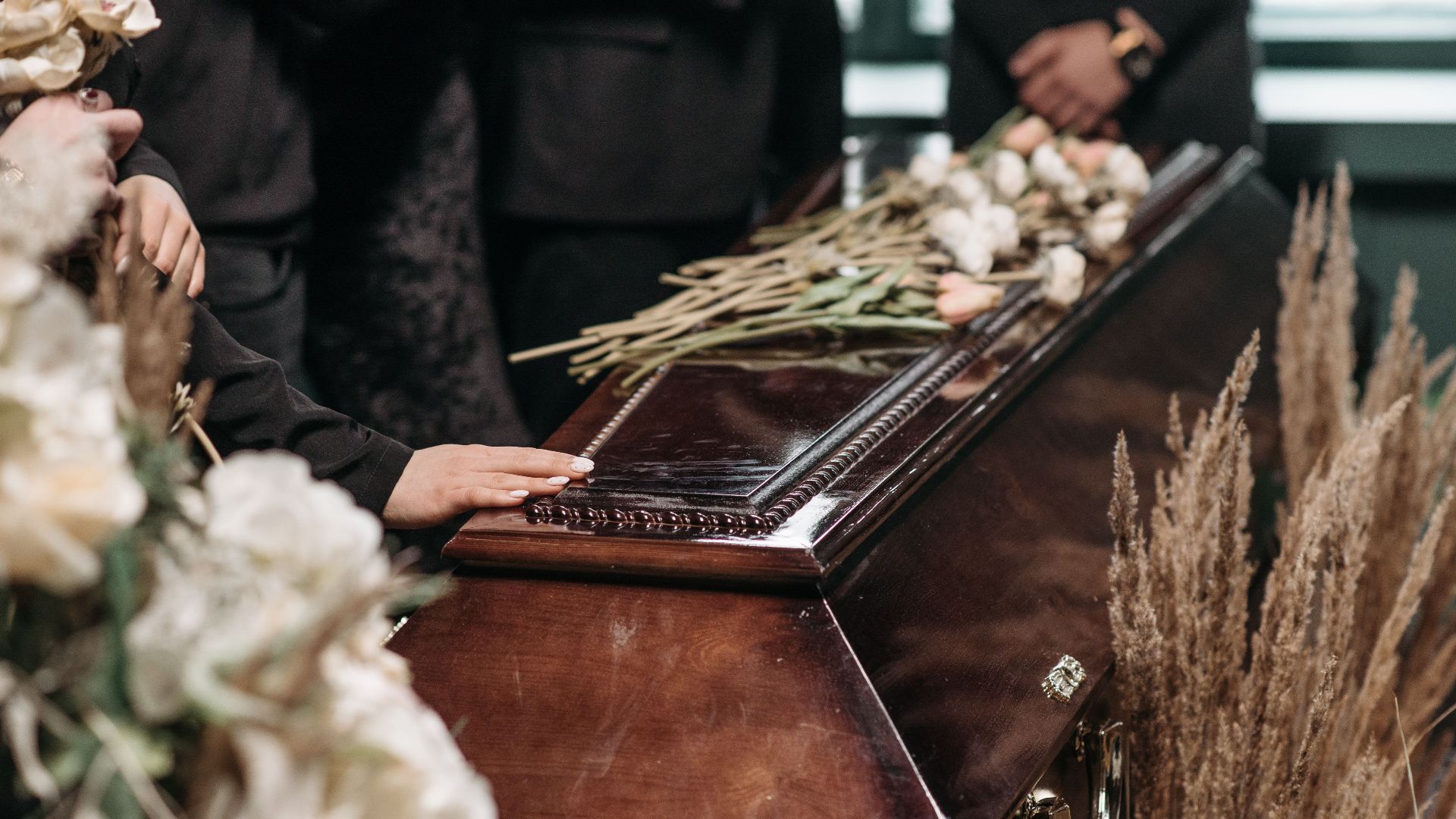 A poignant funeral moment with mourners gathered around a coffin decorated with flowers.