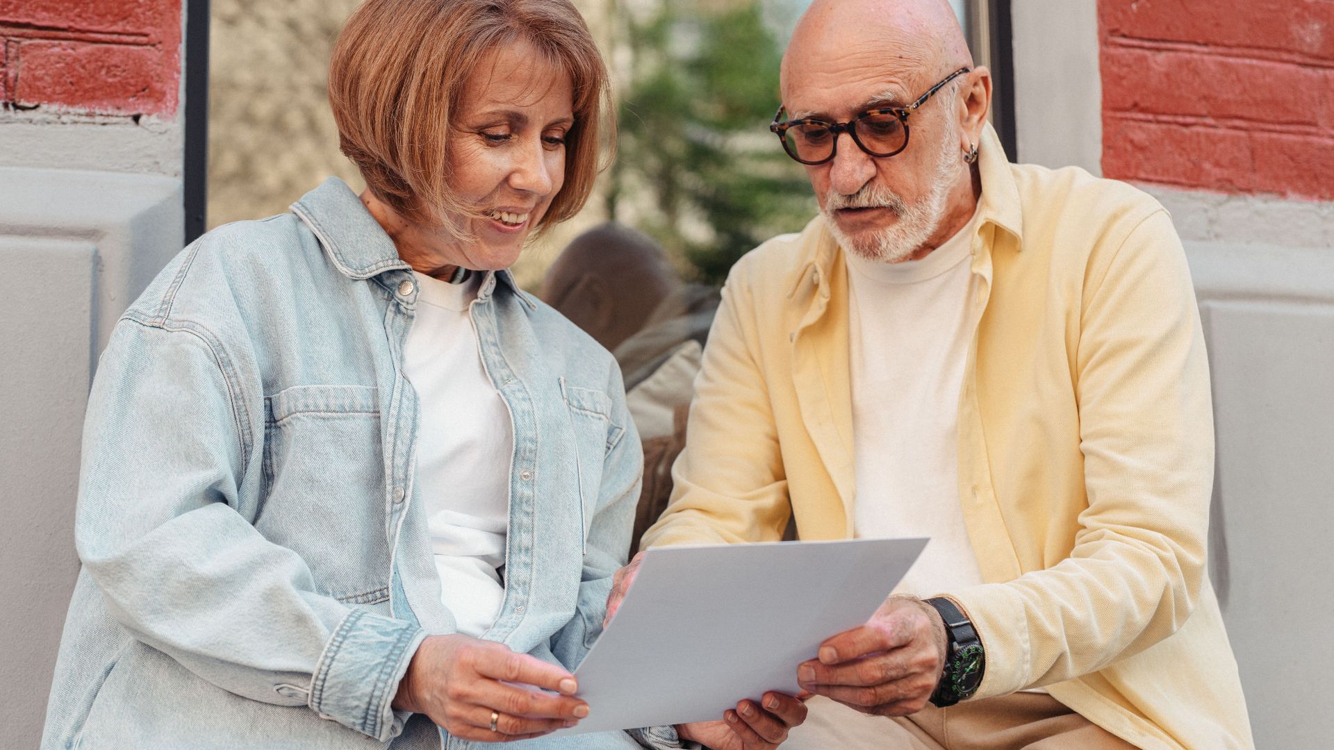 Elderly couple reading a document together while sitting outside at a cafe.