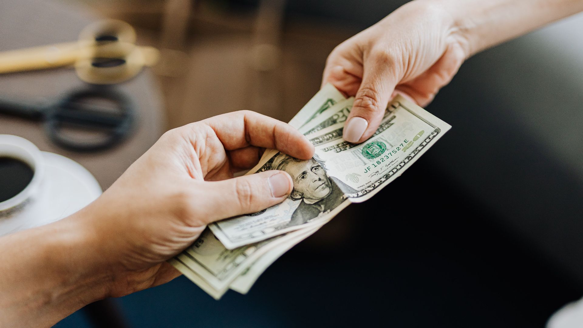 A close-up image of hands exchanging US dollar bills, symbolizing financial transaction or payment.
