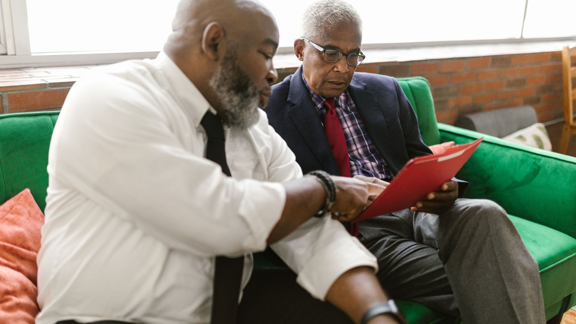 Two men discussing documents on a green sofa in a business setting.