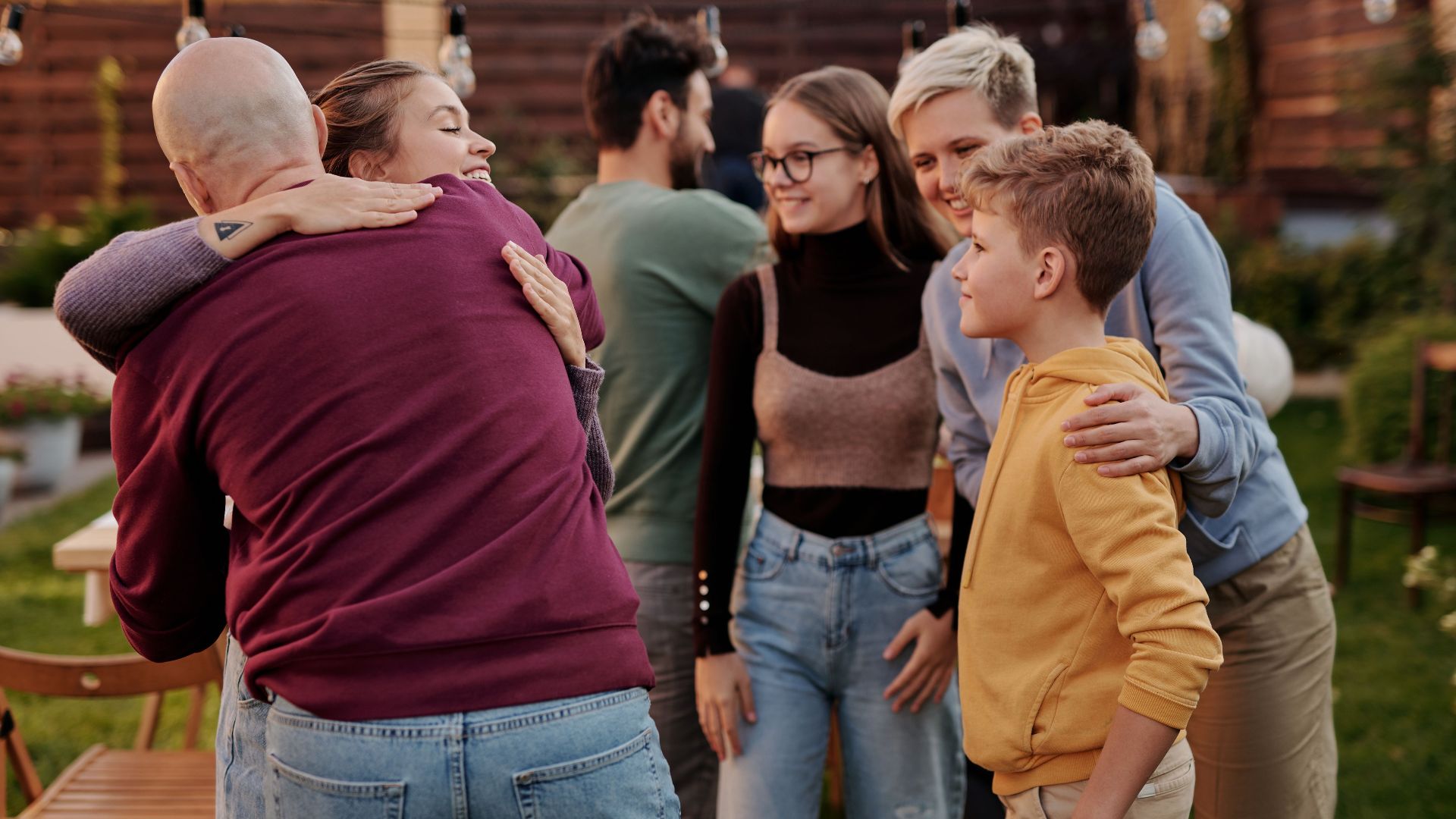 Cheerful group of people hugging each other while spending weekend together in backyard of house