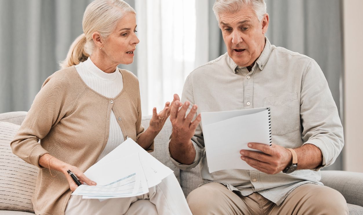 Stress, old couple with documents and taxes in home, mortgage payment and retirement funding crisis. Financial budget, senior man and woman on sofa with anxiety for bills, life insurance and debt.