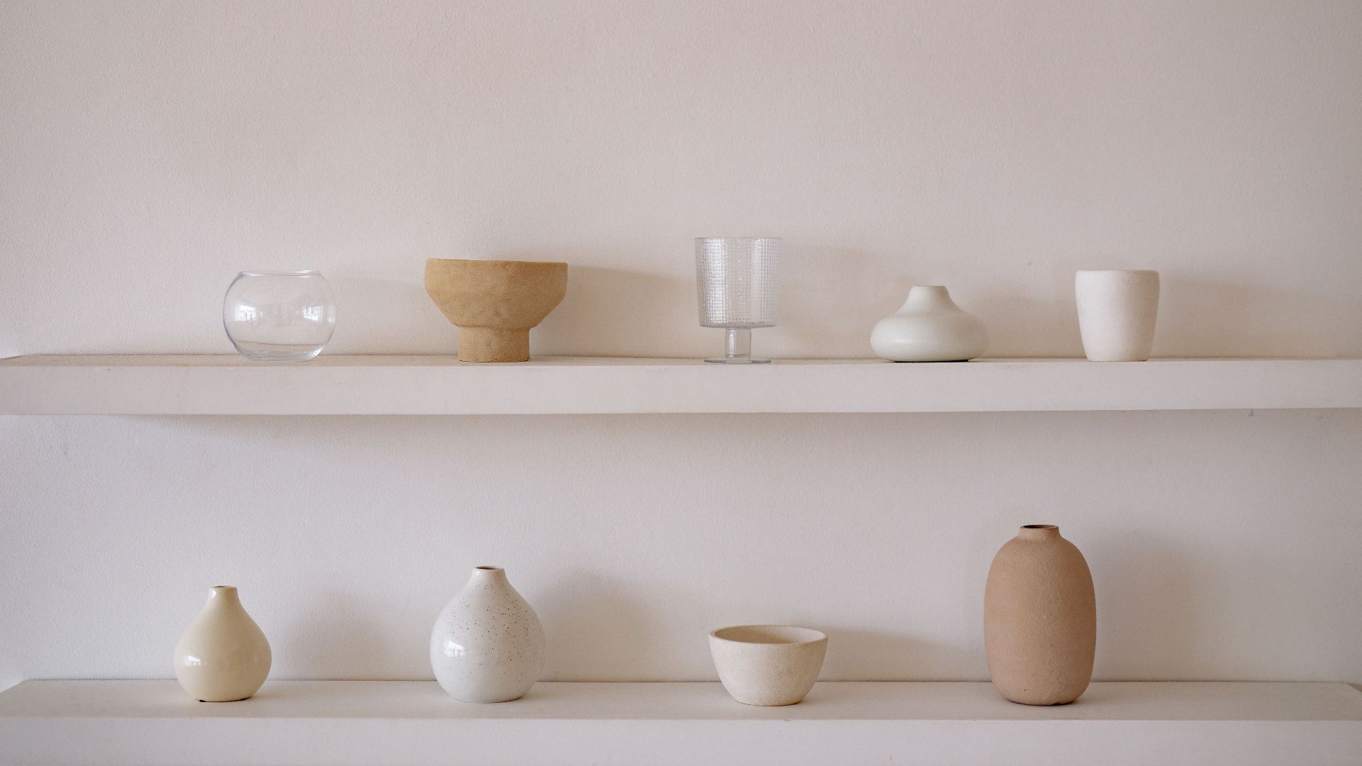 Elegant arrangement of ceramic and glass vessels on minimalist shelves within a neutral indoor setting.