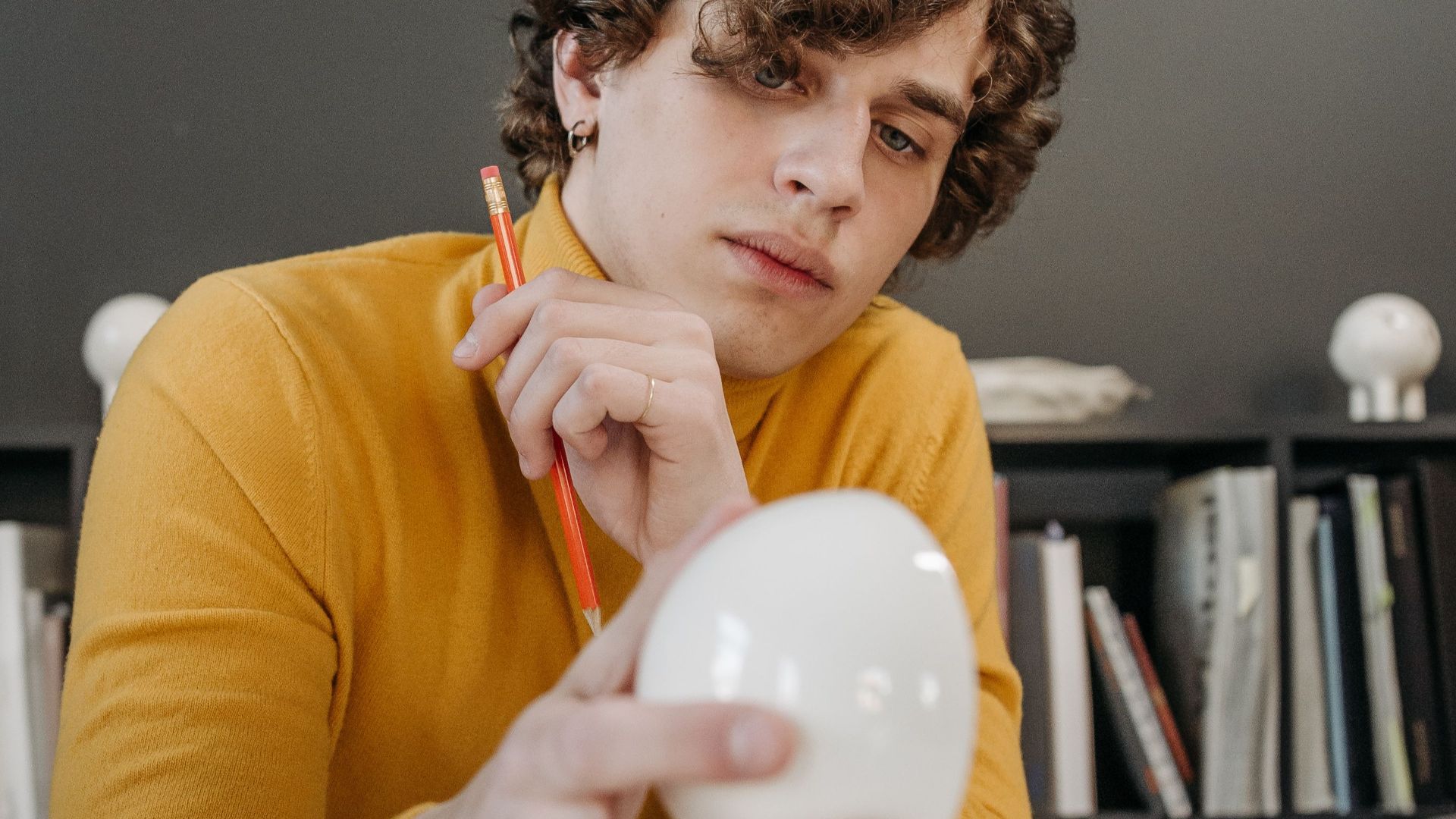 Designer examining ceramic items at a marble-topped desk with tools and plans around.