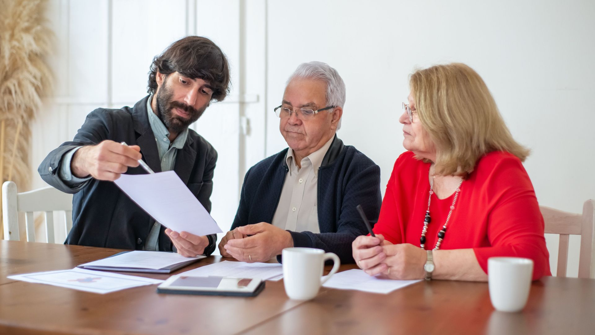 Elderly couple discussing documents with advisor at a wooden table indoors.