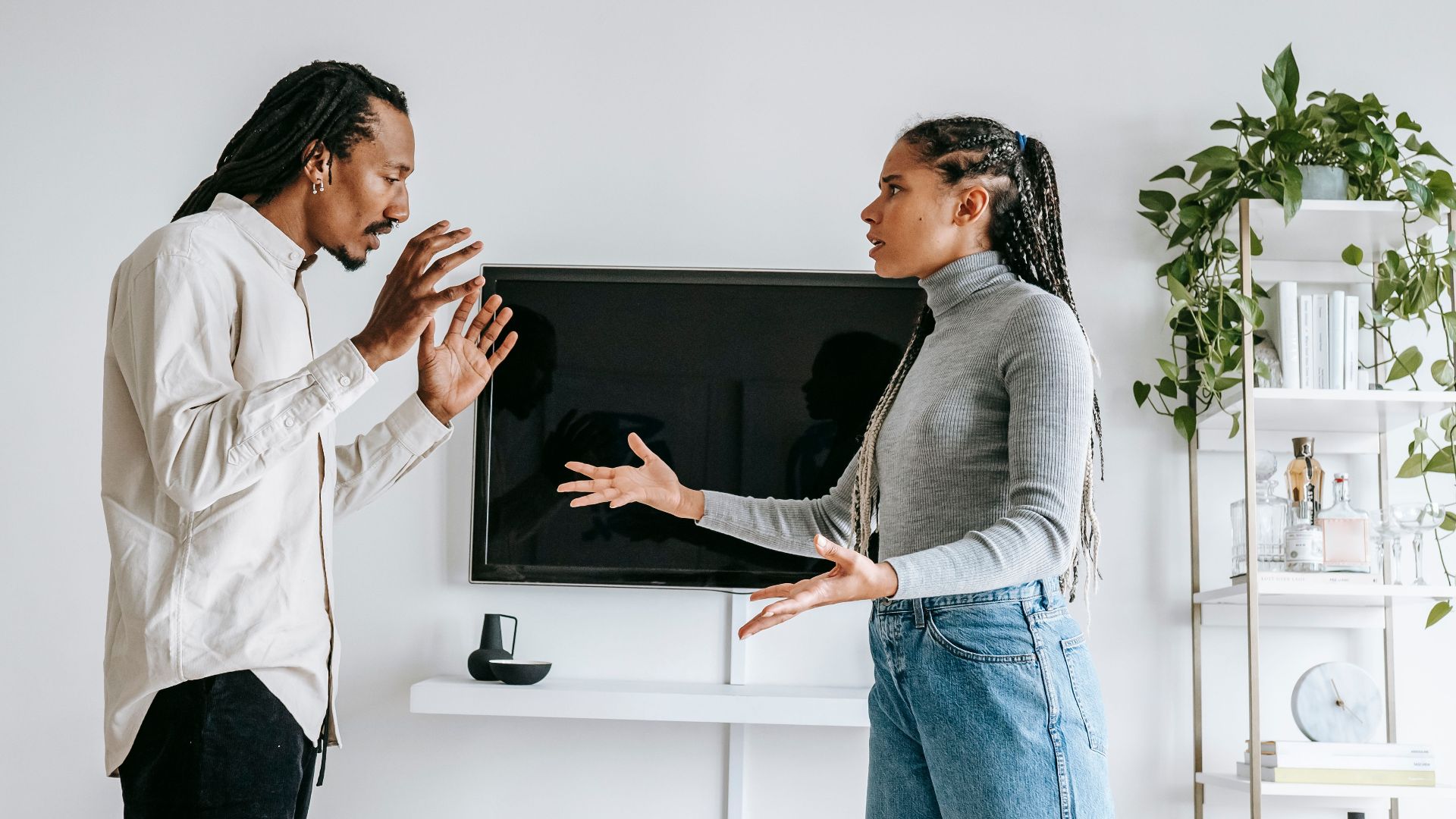 Side view of young African American female in casual outfit gesticulating expressively while arguing with frustrated husband in modern living room