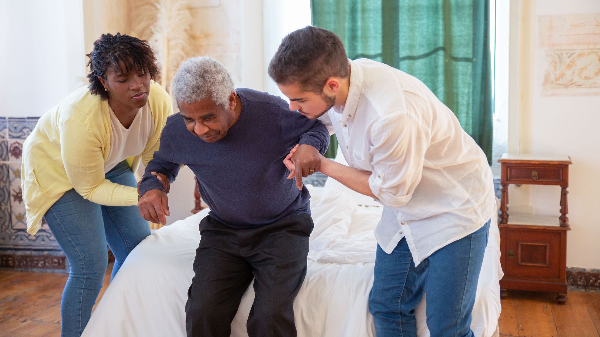 An elderly man receiving assistance from caregivers in a cozy home environment.
