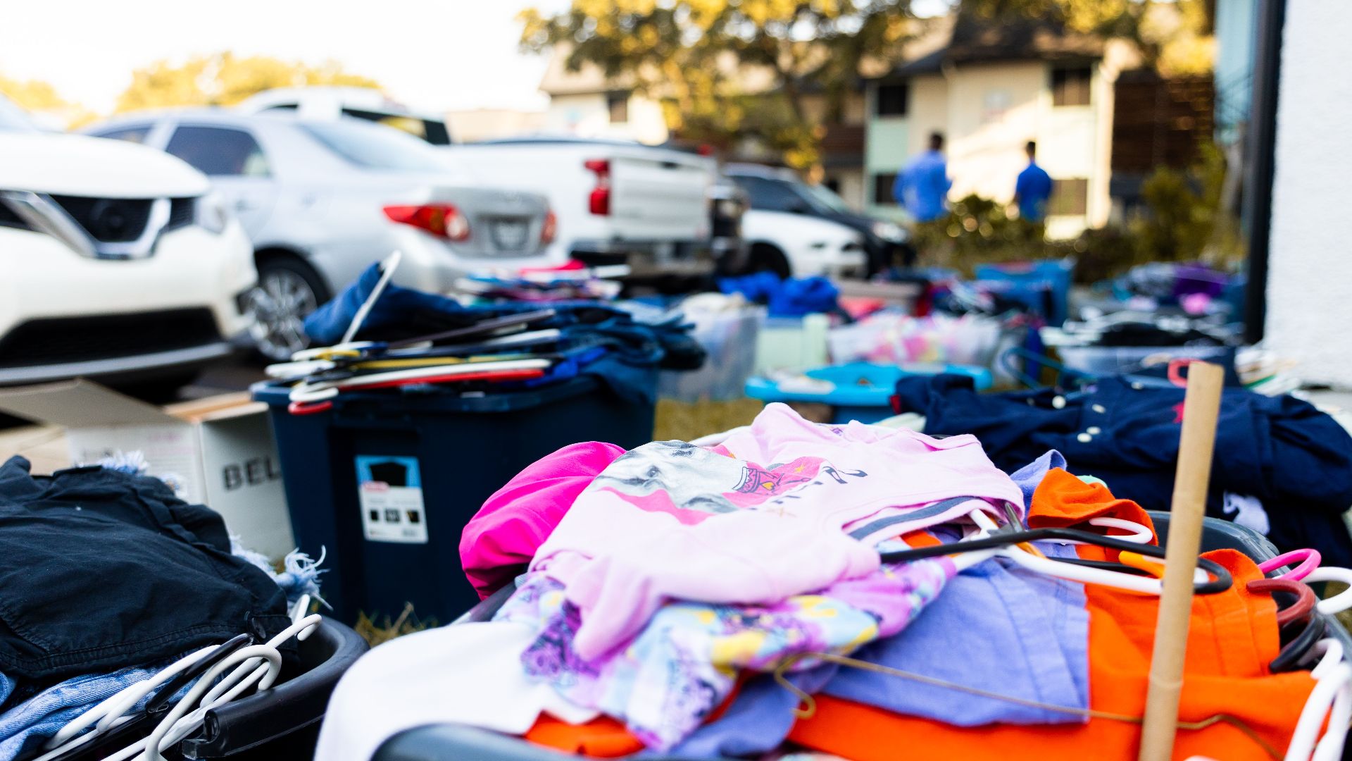 An outdoor garage sale featuring various clothes and cars in a suburban setting.