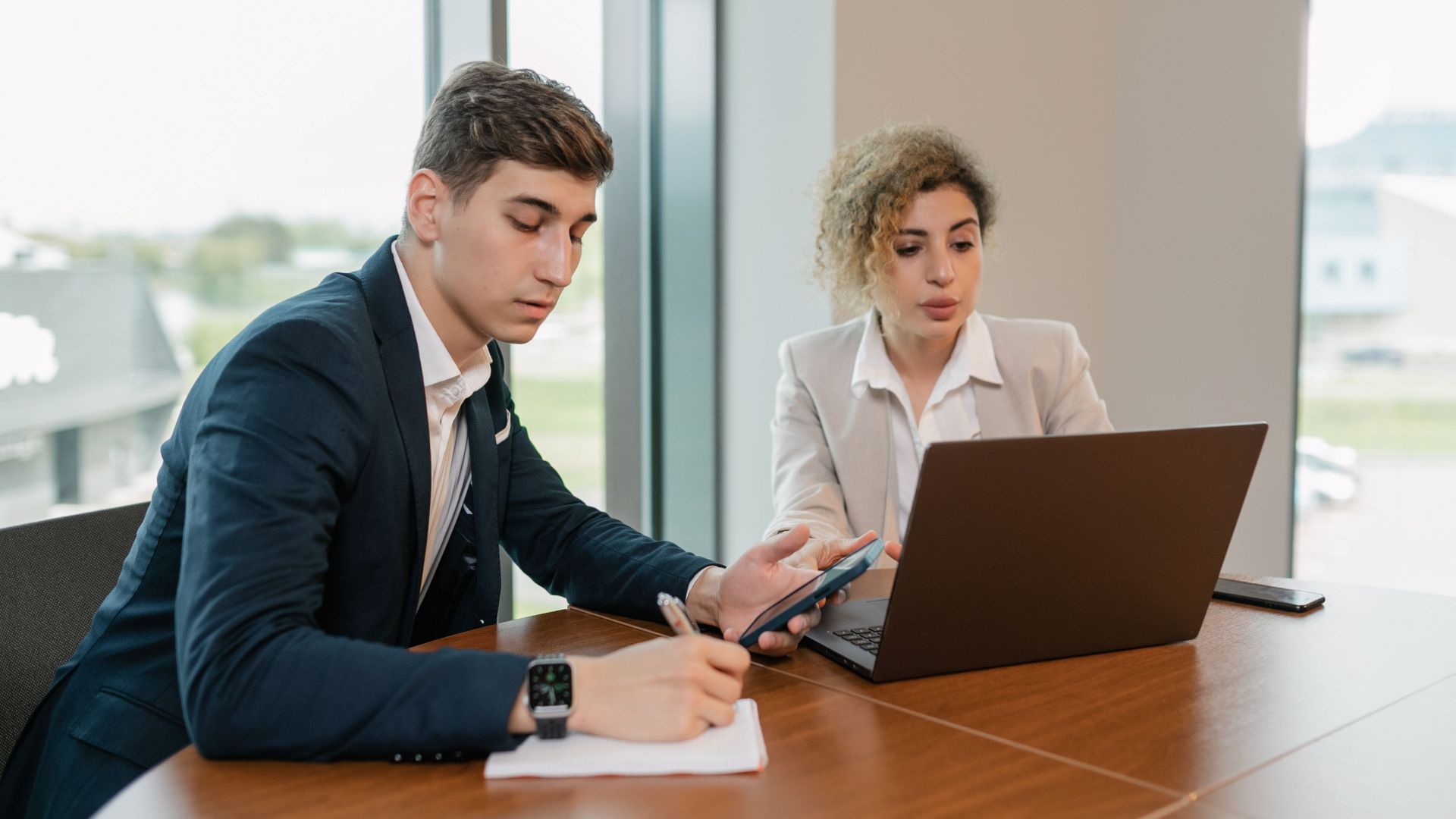 Corporate professionals collaborating with laptop and phone in a modern office setting.
