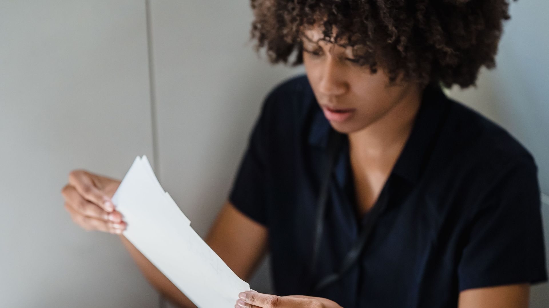 Adult woman examining papers while seated in an office corner.