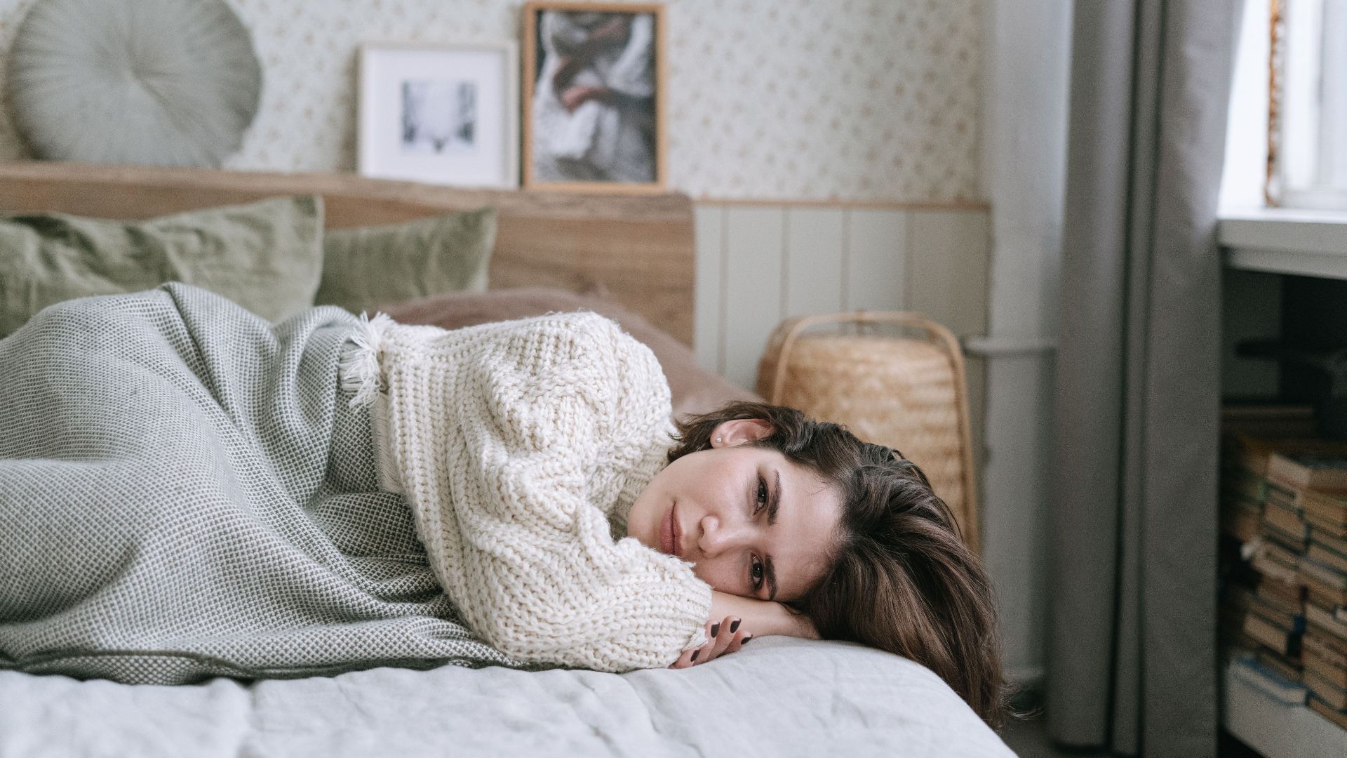 A woman in a knitted sweater lies on a bed, creating a cozy atmosphere.