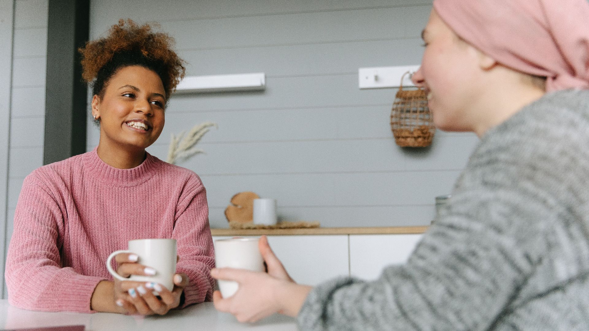 Two women share a joyful coffee moment at home, embodying friendship and warmth.